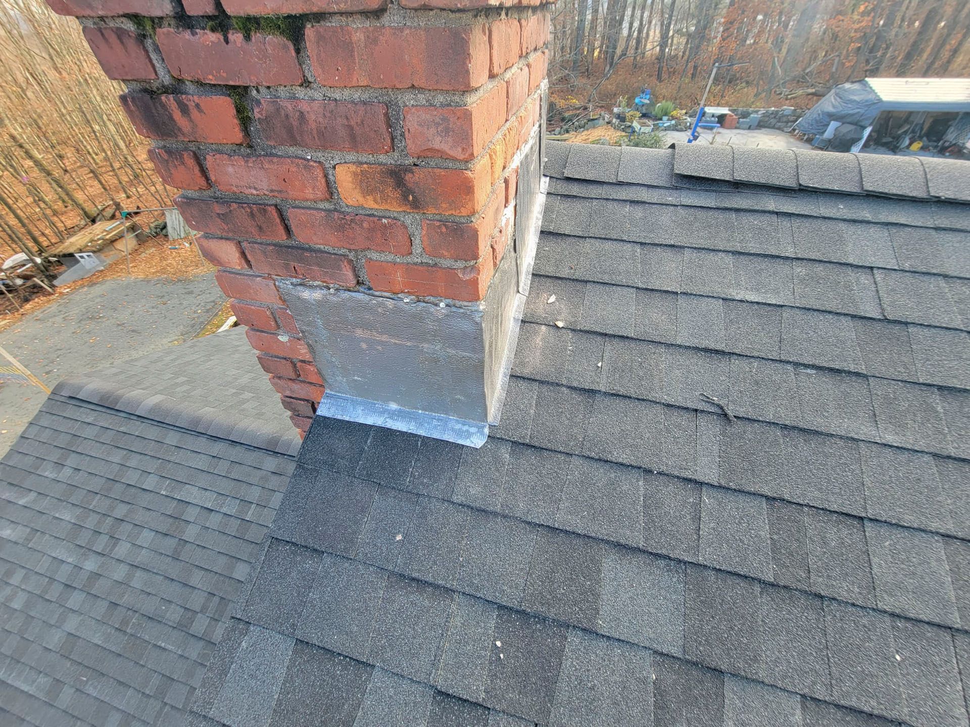 Roof shingles and brick chimney with flashing, viewed from above on a sloped rooftop