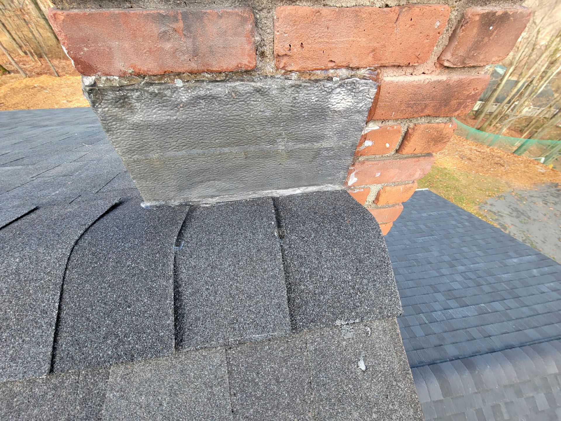 Close-up of a roof shingle intersection beneath a brick wall and gray stone ledge.