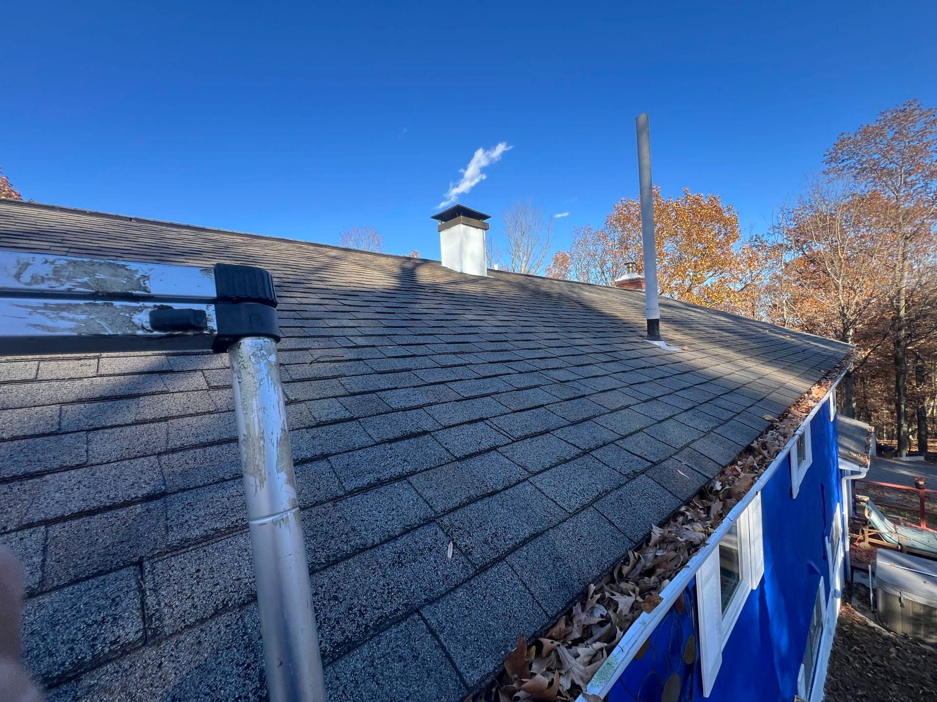 Rooftop with gray shingles, chimney, and a blue-painted wall under a clear blue sky