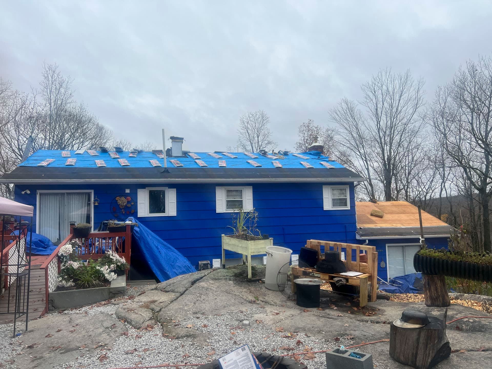 Blue house with damaged roof, debris in yard, and a blue tarp over the front steps