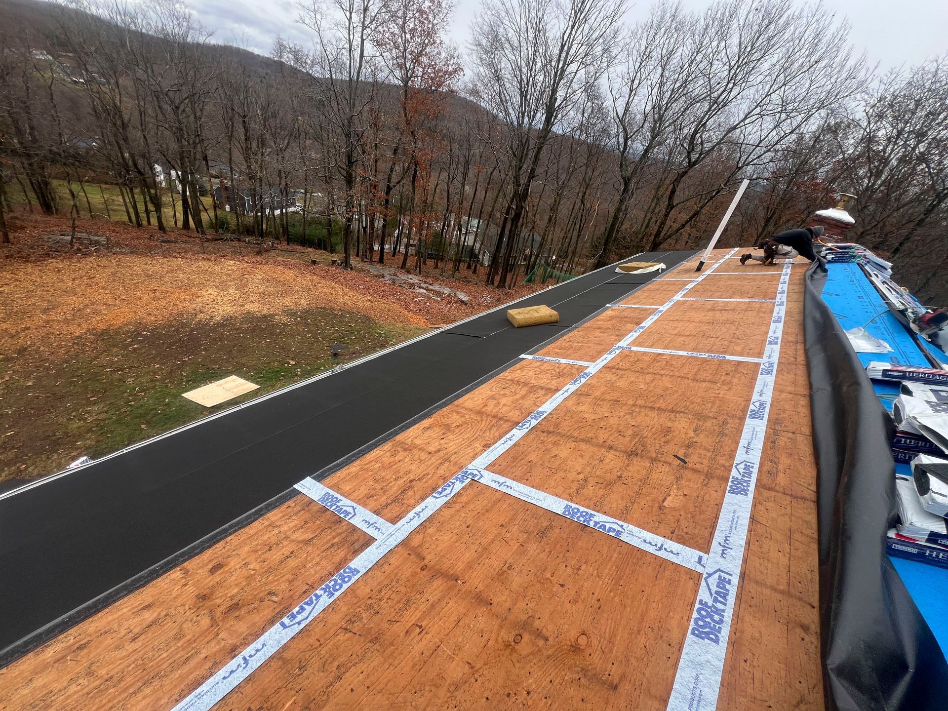 Long wooden rooftop walkway with blue tape markings beside a black path in a wooded area