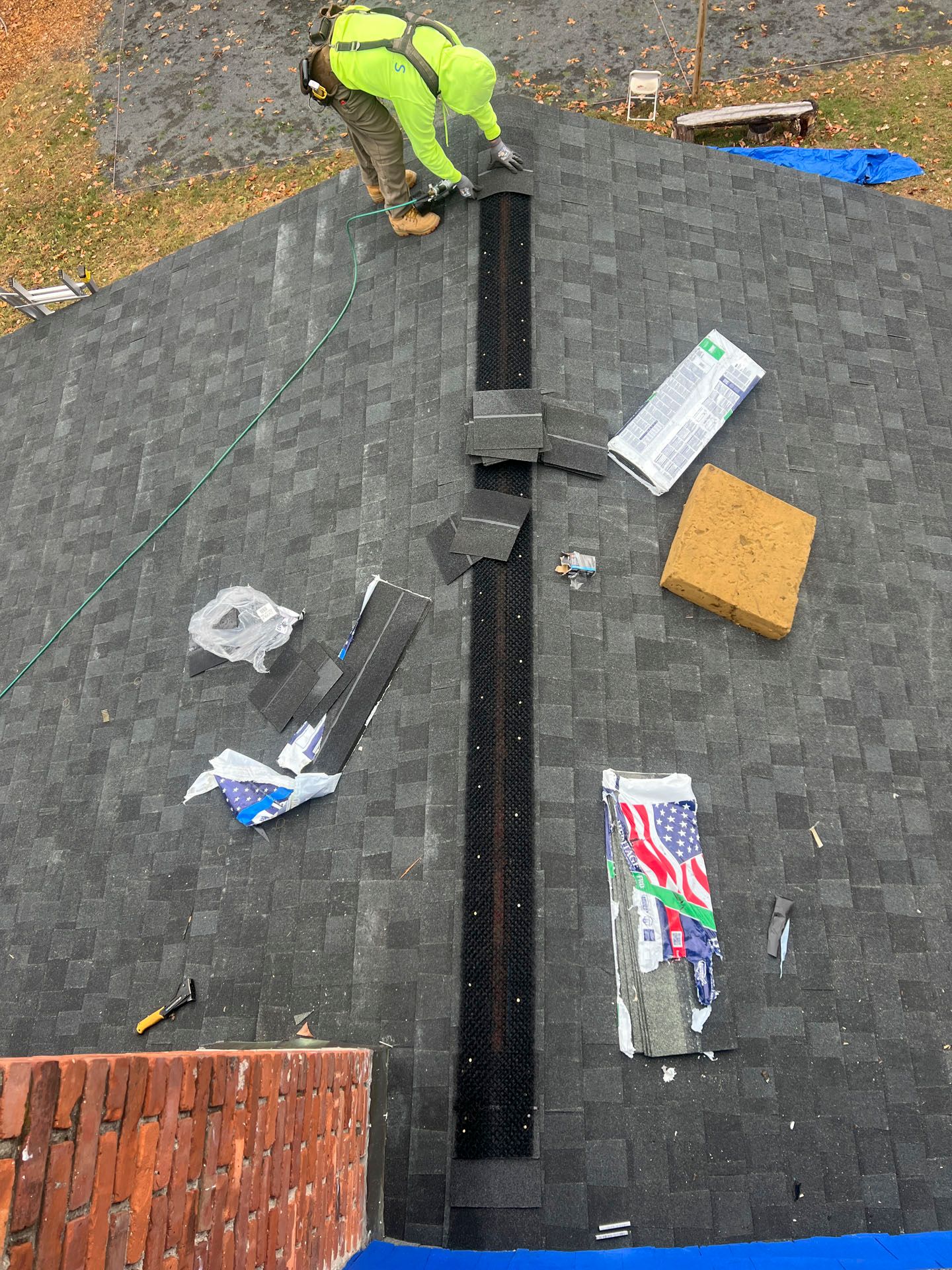 Worker installing shingles on a roof, with materials and tools scattered around a dark gray roof surface.