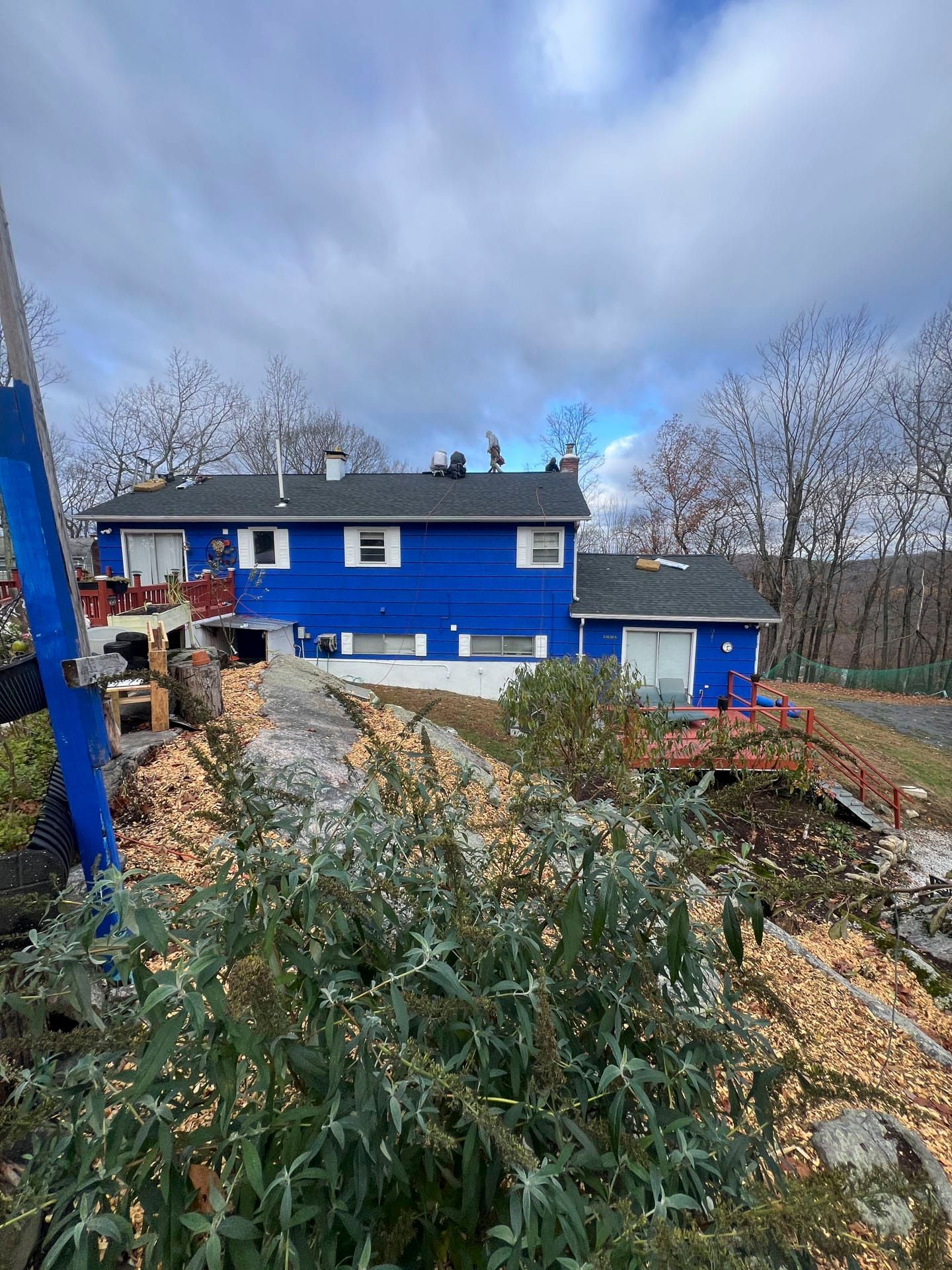 Blue house with white trim beside a gravel driveway and trees under a cloudy sky