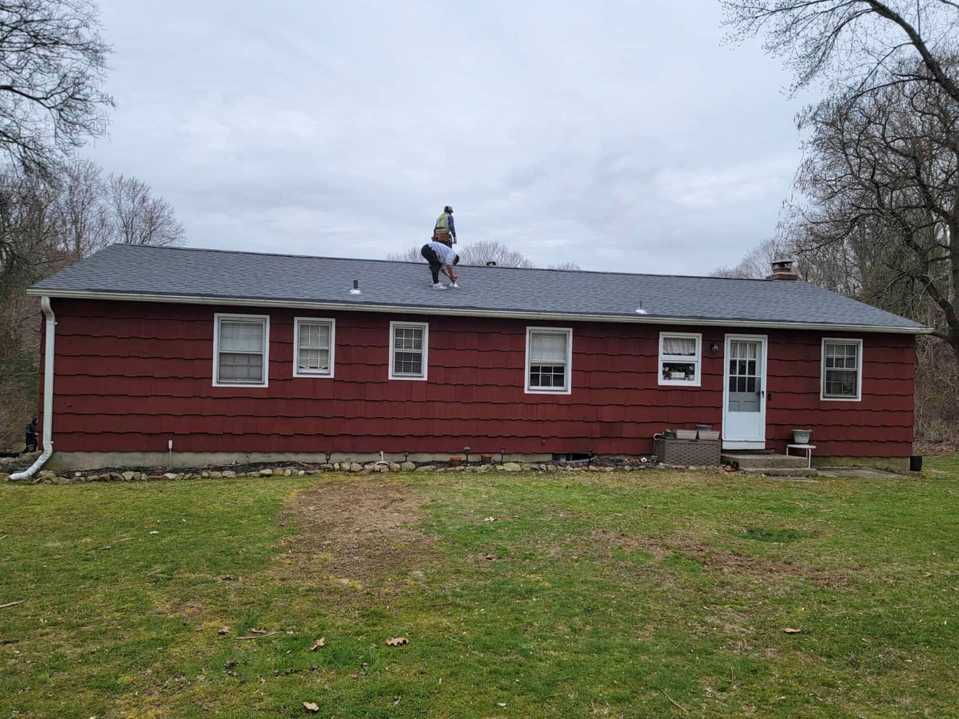 Person on the roof of a red house with a white door and windows, under a cloudy sky