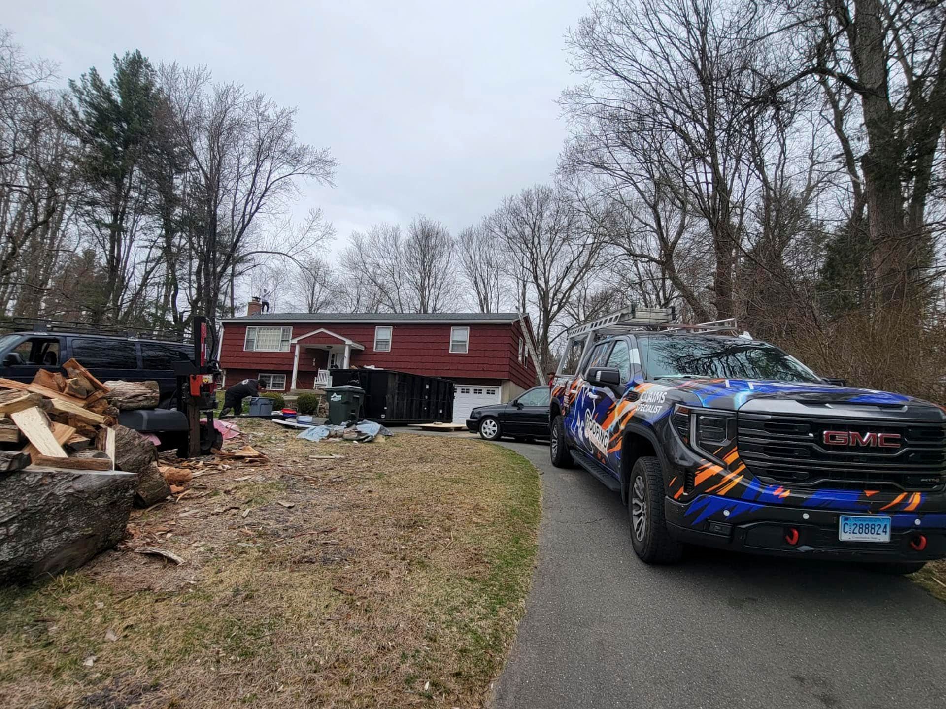 Truck with colorful wrap in front of a red house, with debris and trees after a storm.