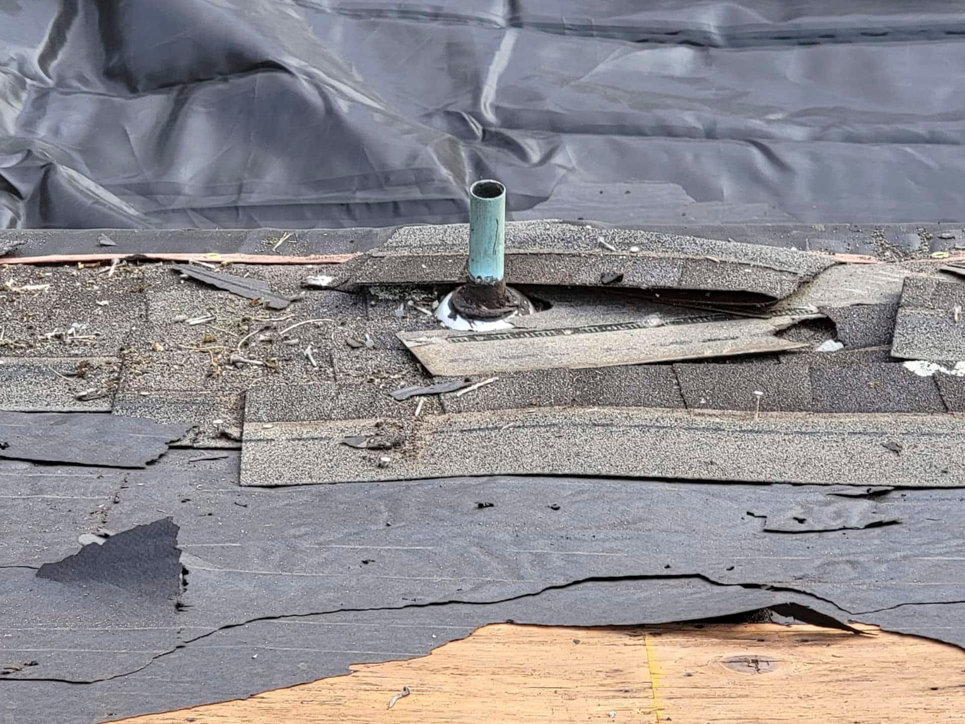 Damaged rooftop with torn black waterproof membrane and a small green vent pipe exposed in the center.