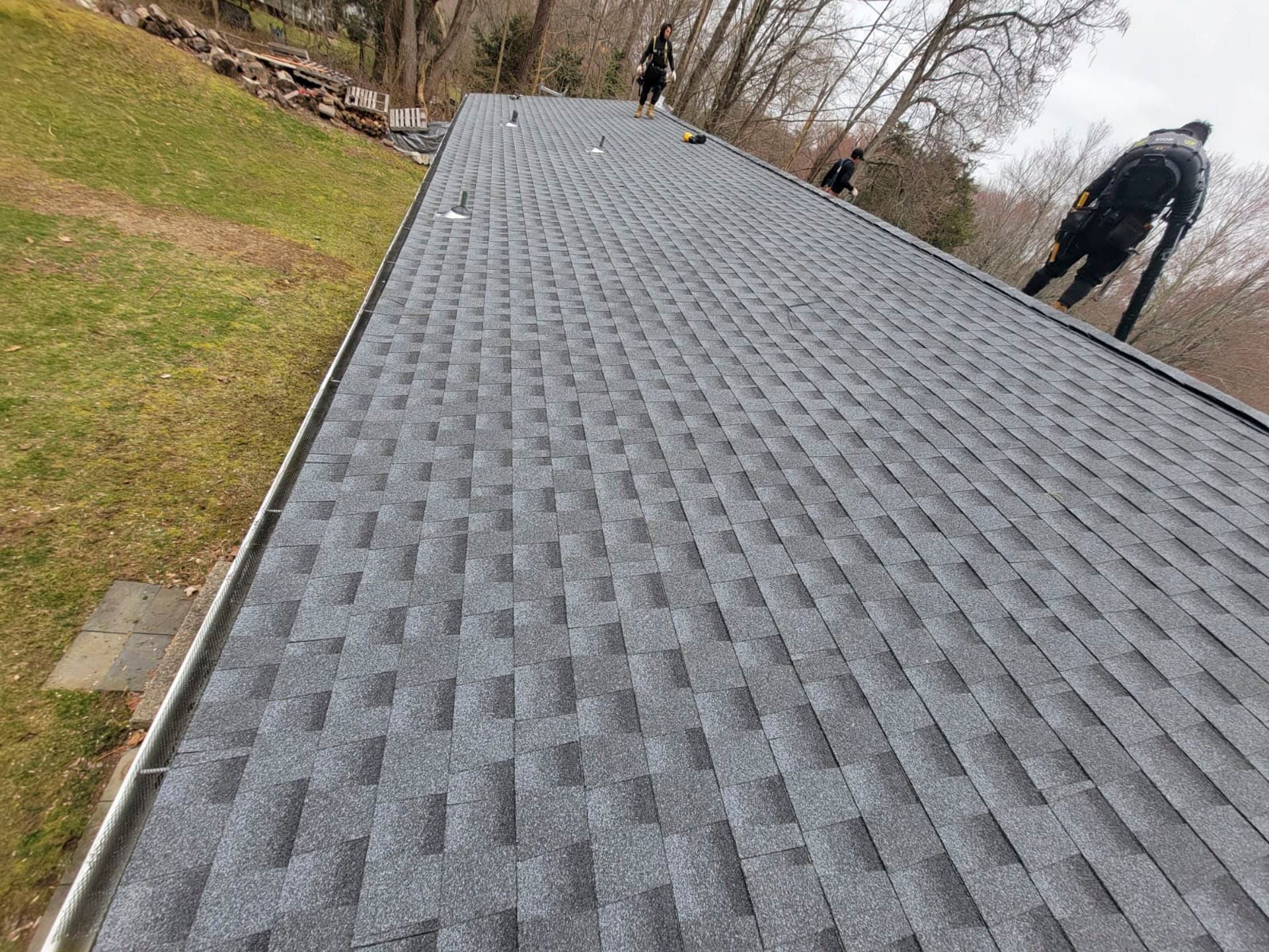 Steep shingled roof with two people standing near the top on an overcast day