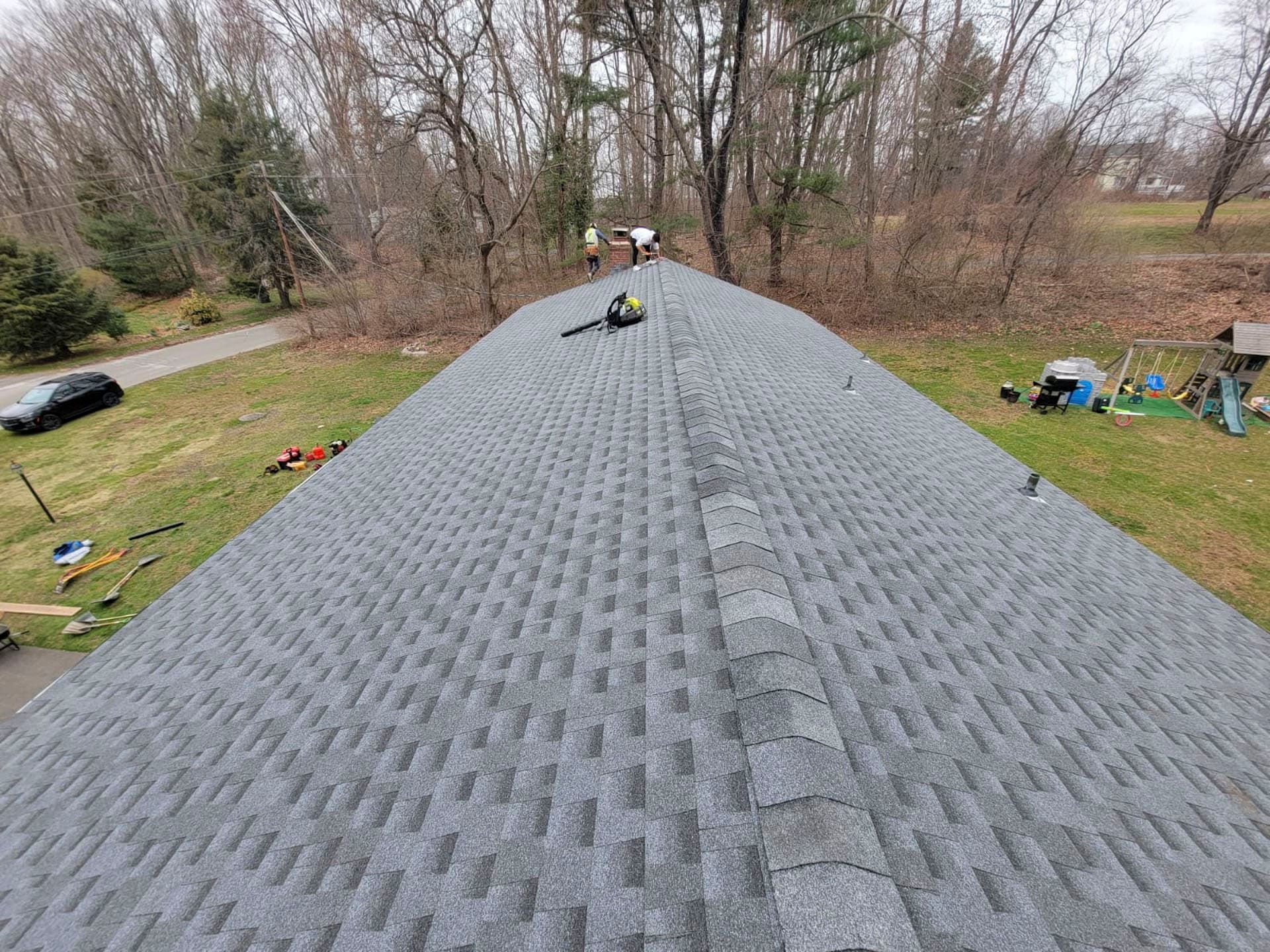 Roof view with gray shingles, a vent, and wooded yard in the background