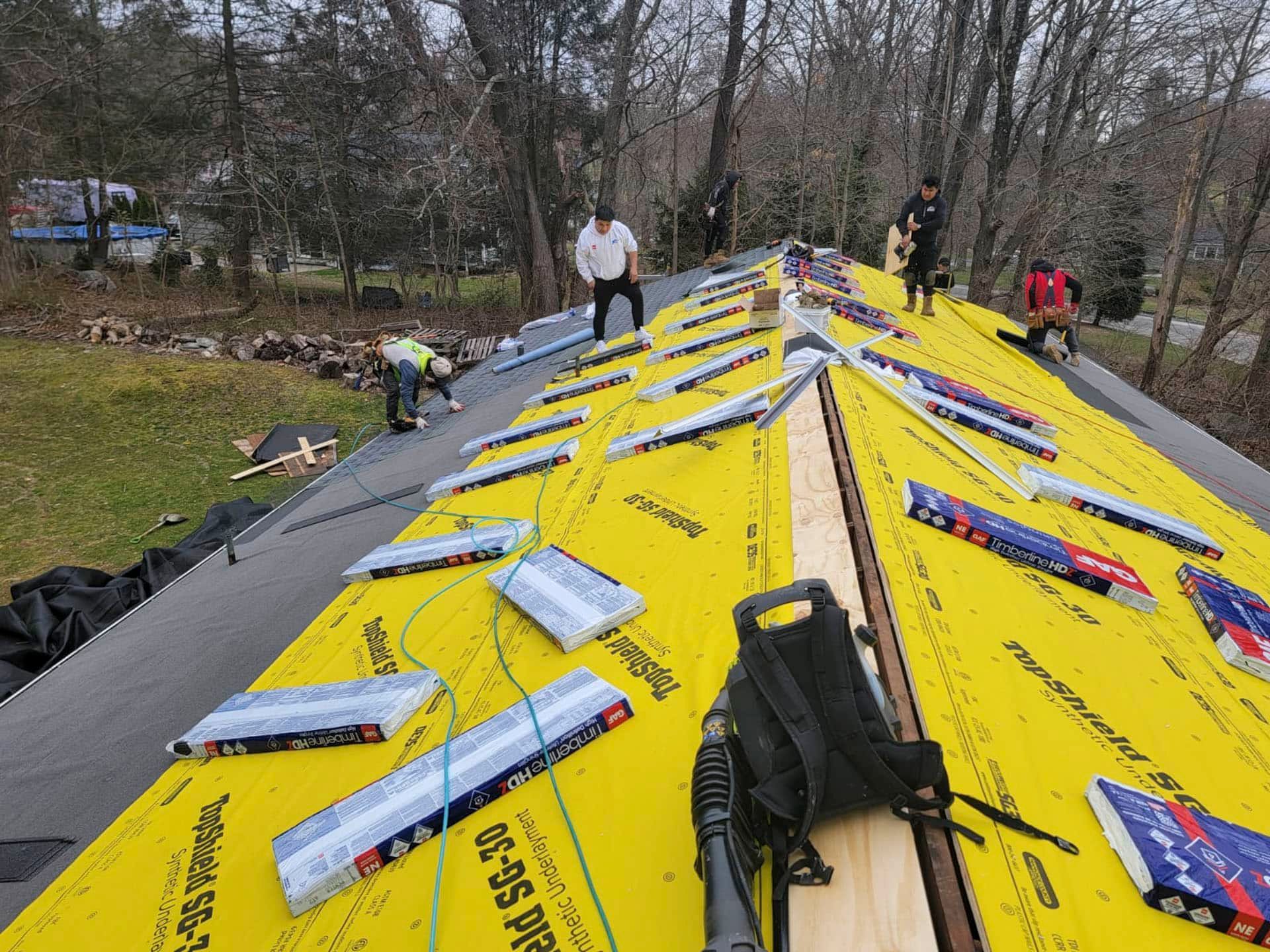 Workers on a yellow roof installing panels, with tools laid out and trees in the background.