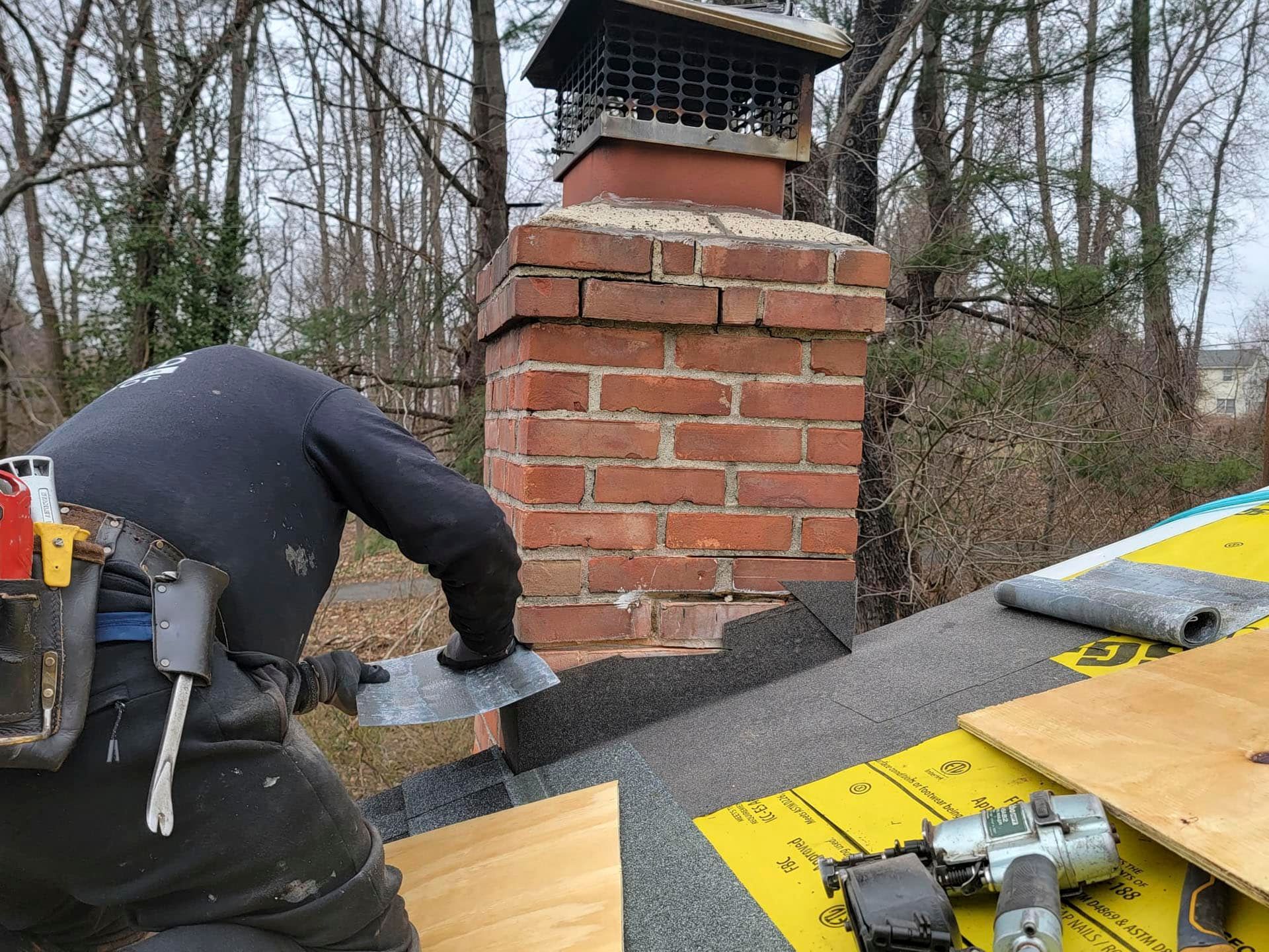 Worker installing roofing on a brick chimney in a wooded area