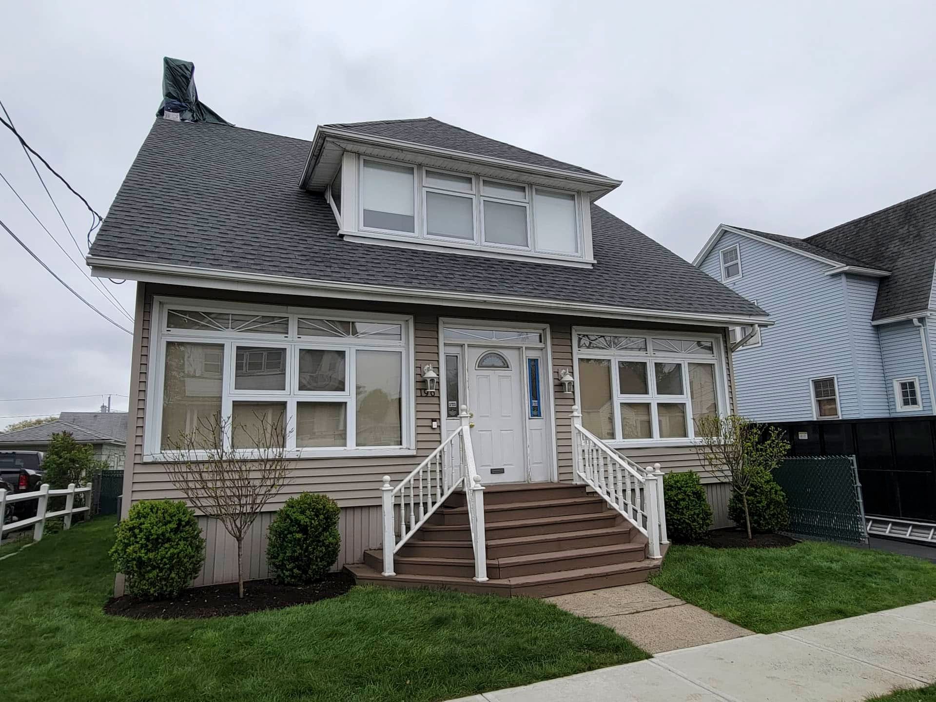 Two-story stone house with steep roof, front steps, and small lawn under cloudy sky