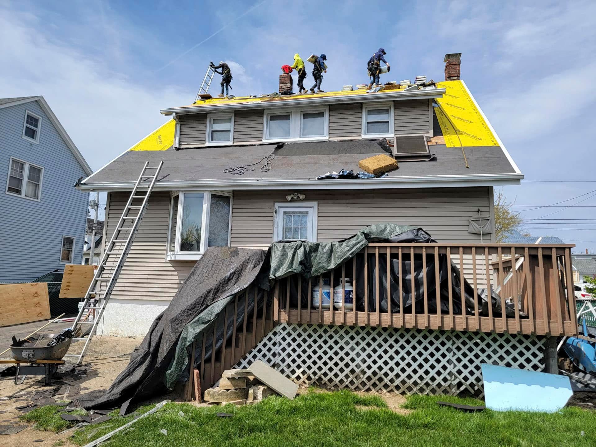 Workers repairing storm-damaged house roof with tarps and exposed shingles