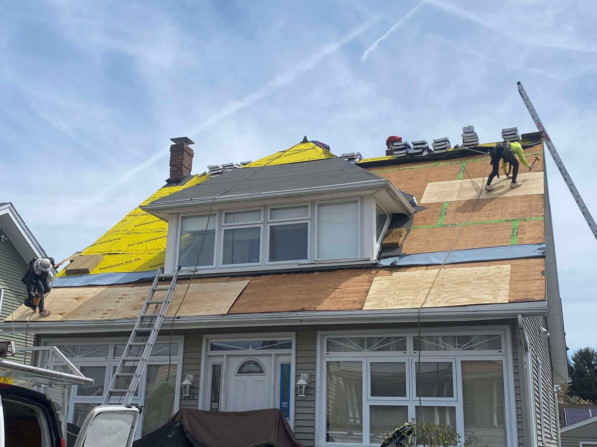 House roof under repair with workers installing yellow underlayment and plywood panels