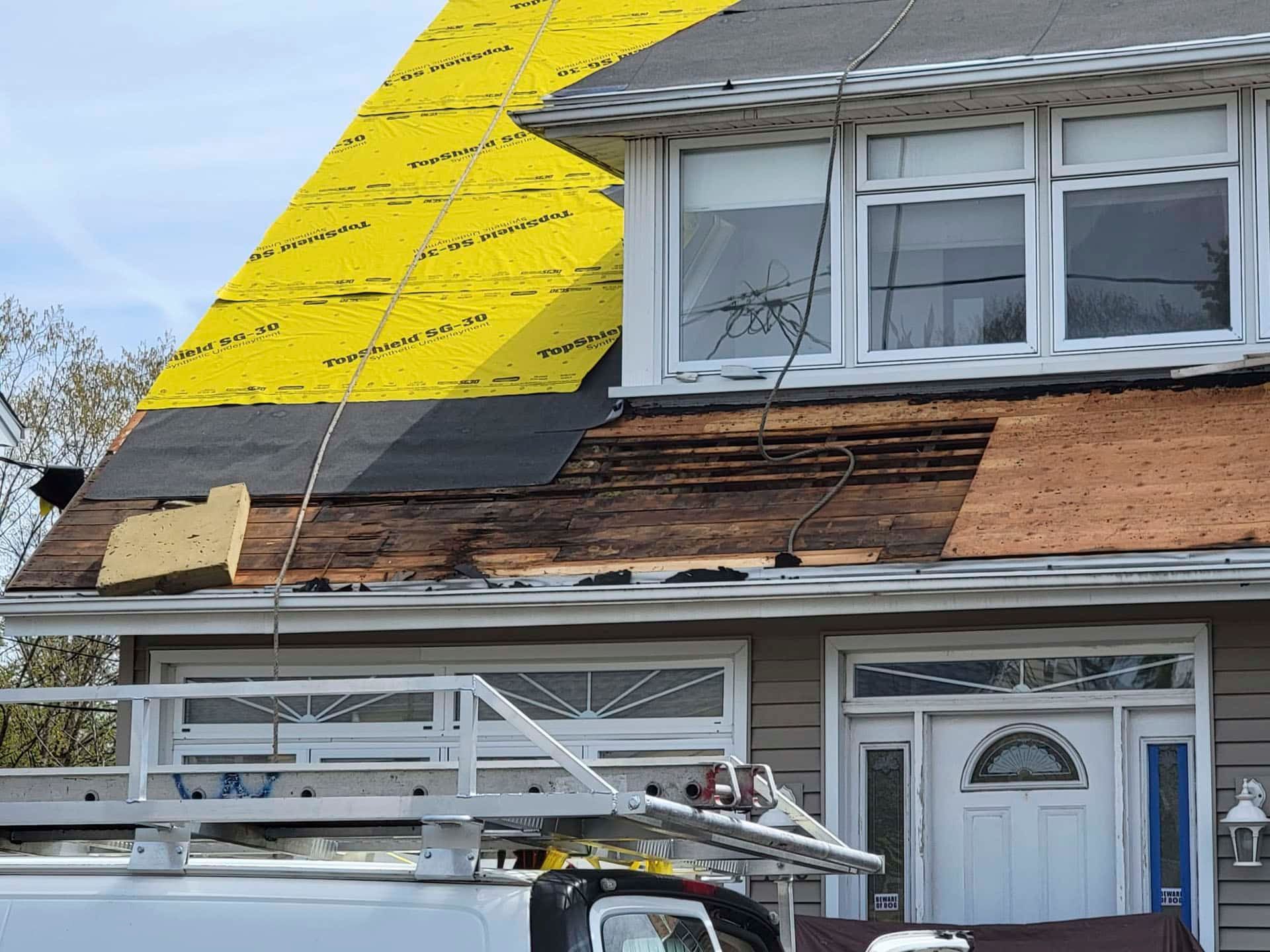 House exterior with workers replacing roof shingles and bright yellow underlayment exposed