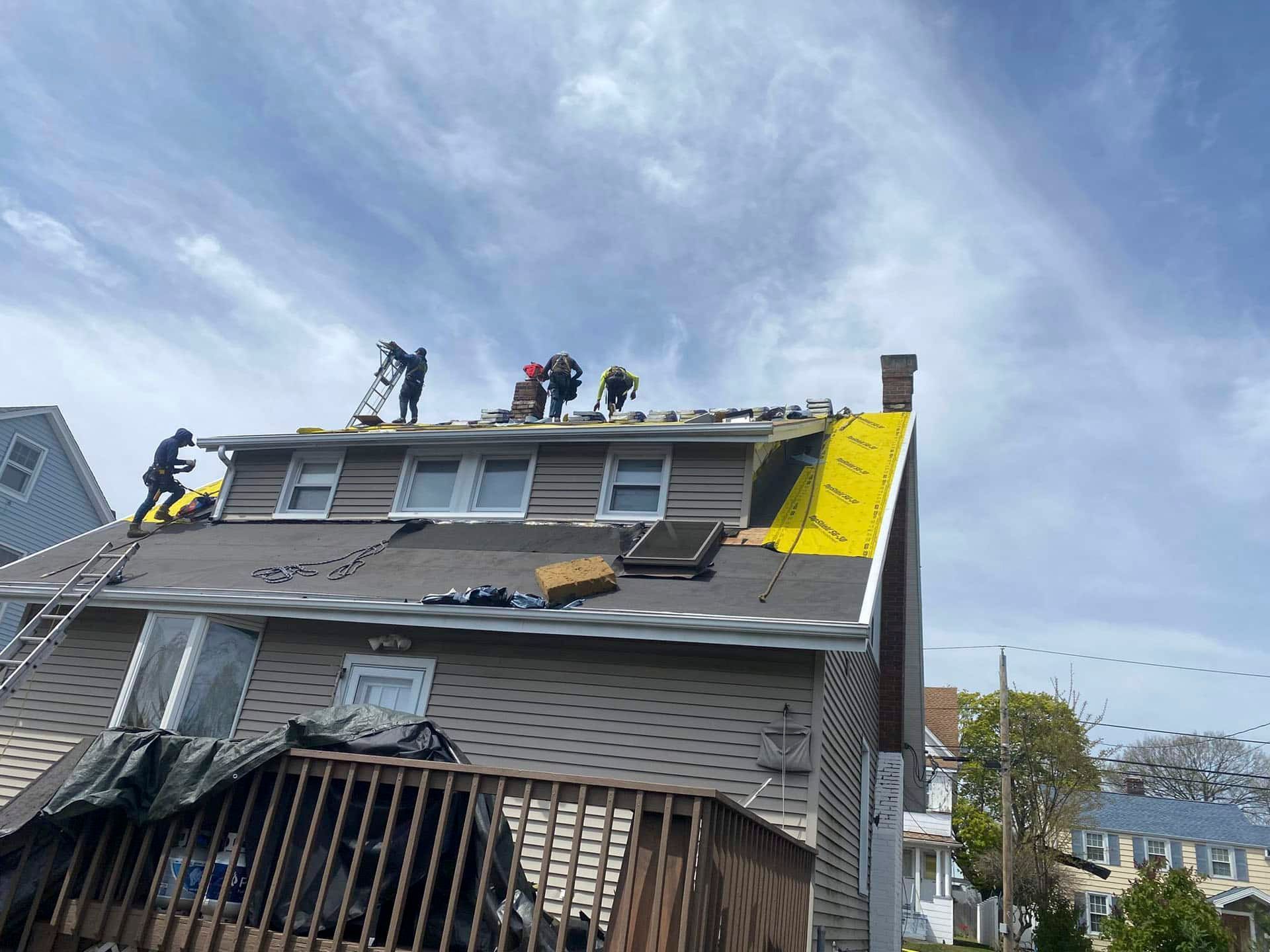 Workers repairing a damaged roof on a tilted house with yellow tarp and debris below