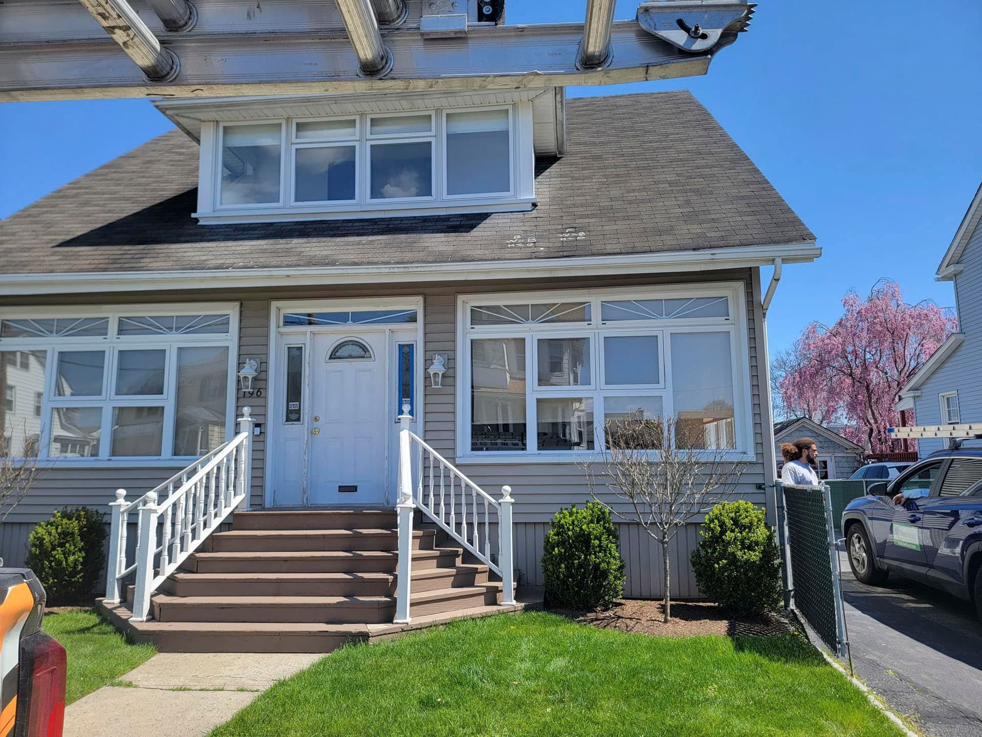 White house with front steps, porch railings, and a dormer under a clear blue sky.