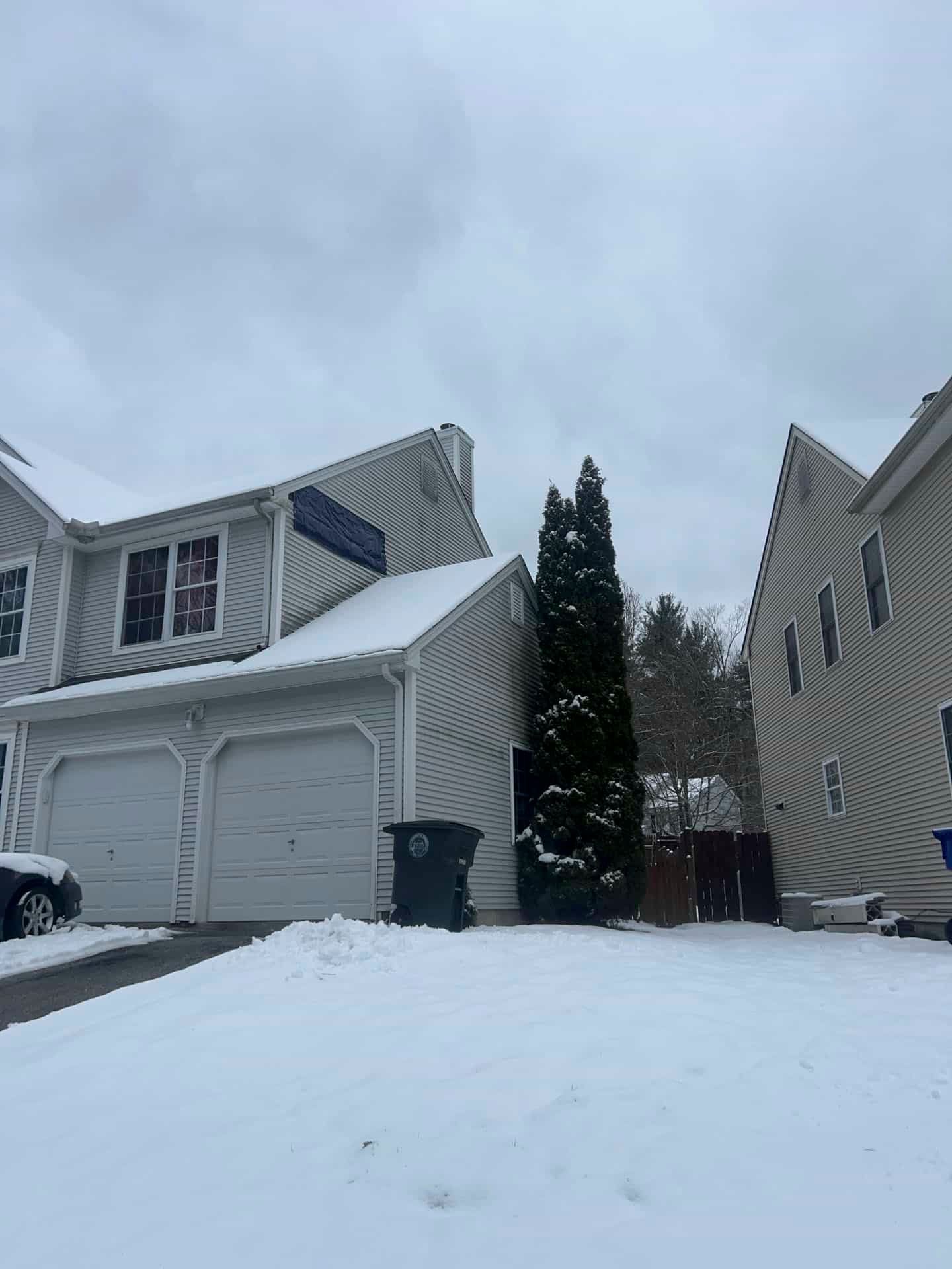 Snow-covered suburban townhouse with garage and driveway under an overcast sky