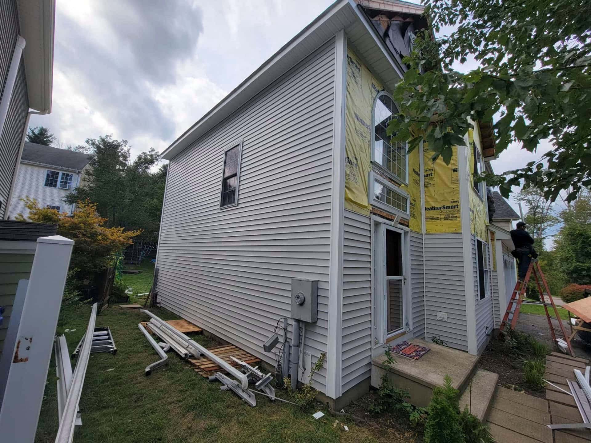White two-story house exterior with siding repairs, scaffolding, and a small front stoop.