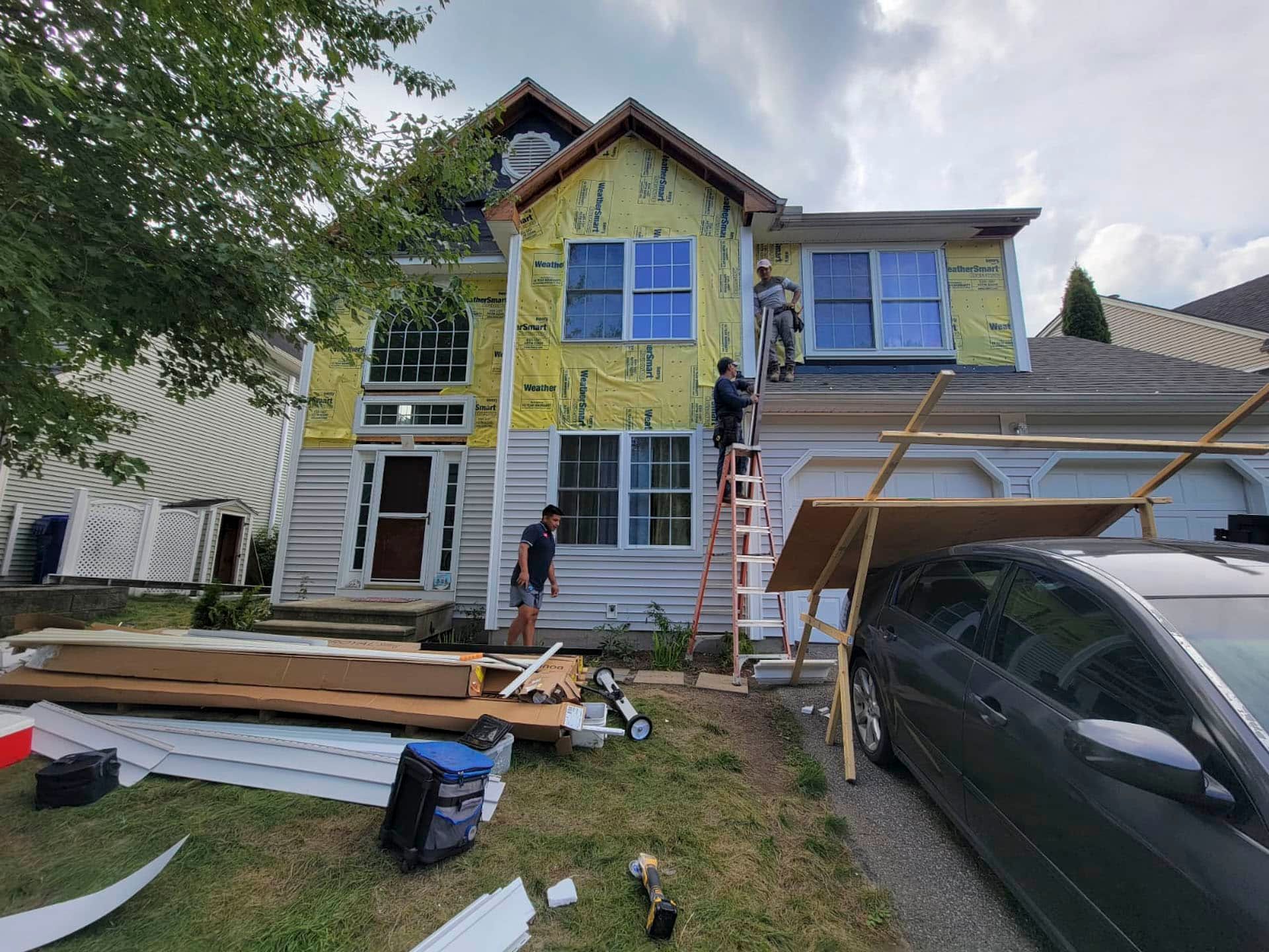 House under renovation with workers on scaffolding and lumber stacked in the driveway