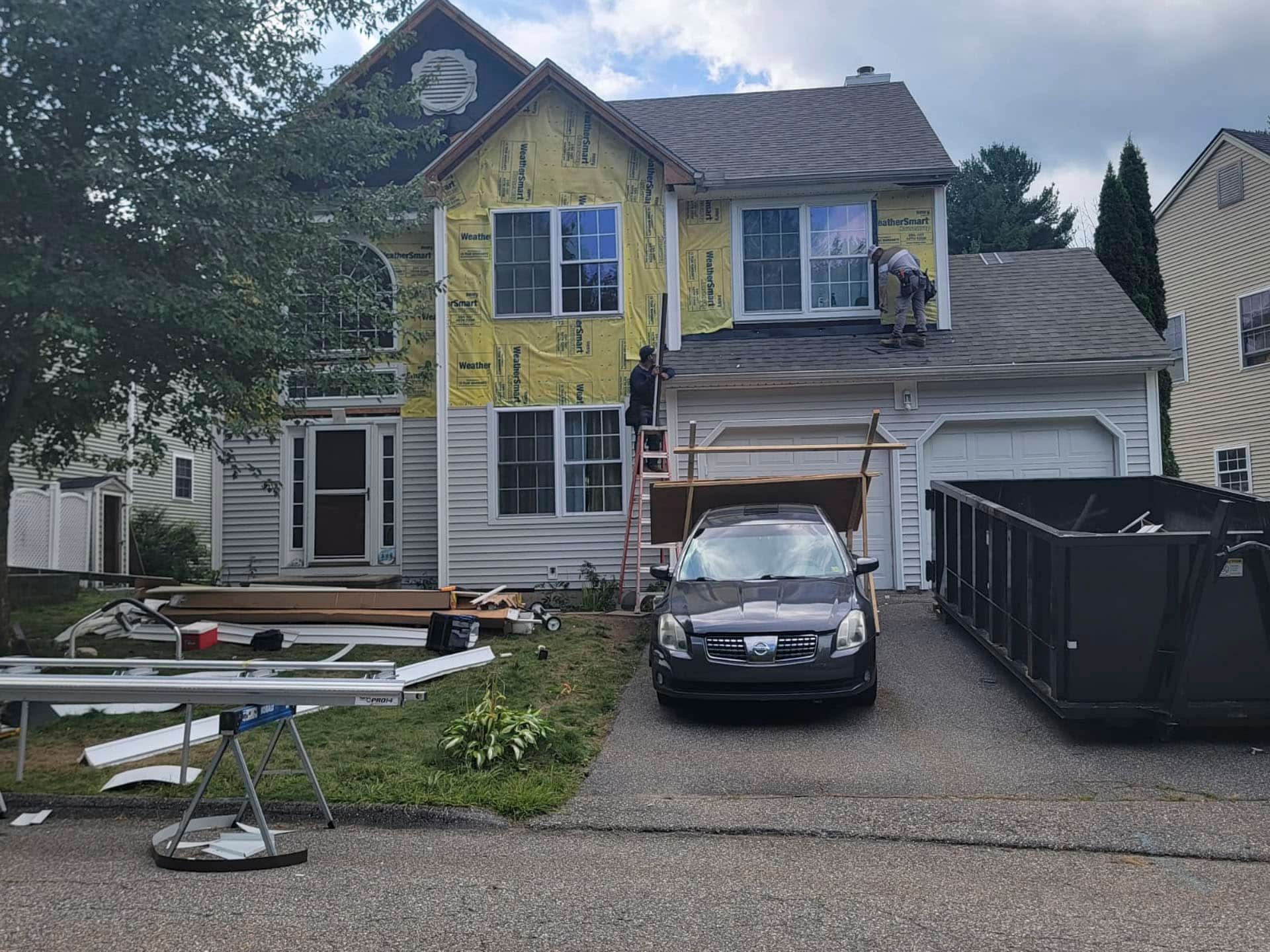 Partially renovated two-story house with yellow siding, parked car, and construction materials in the driveway