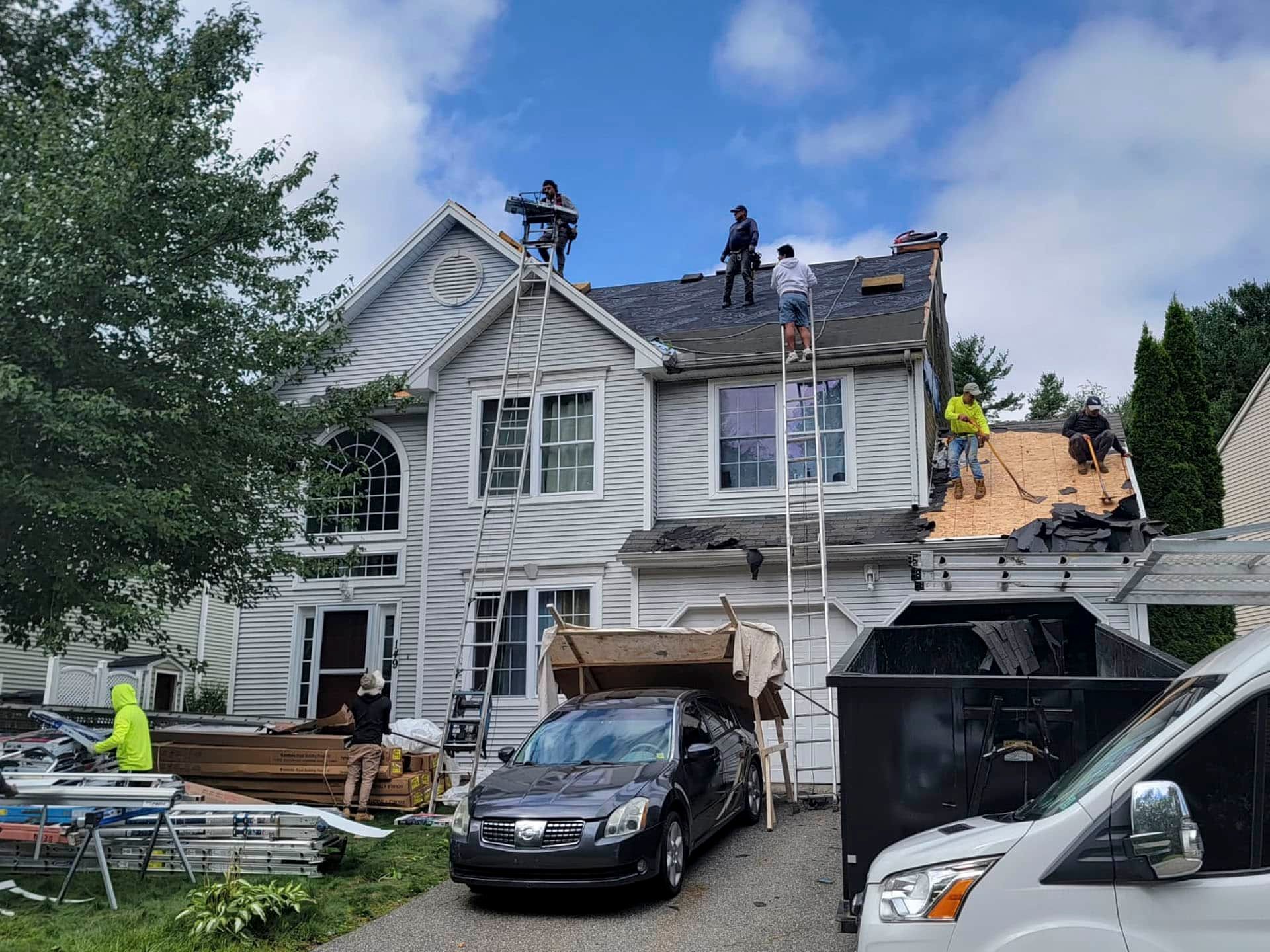 House under roof repair with workers, ladders, and cars in the driveway