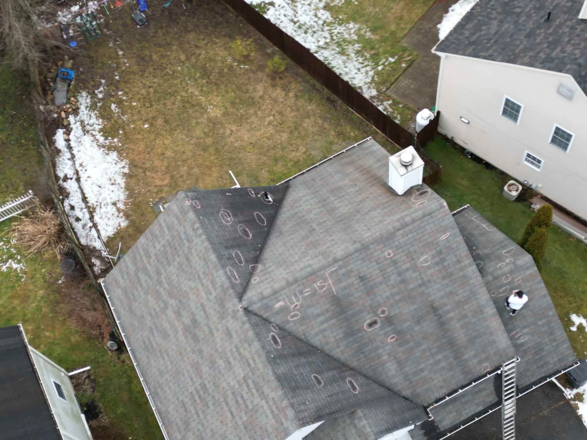 Aerial view of two rooftops beside a snowy backyard and driveway, with trees along the edge.
