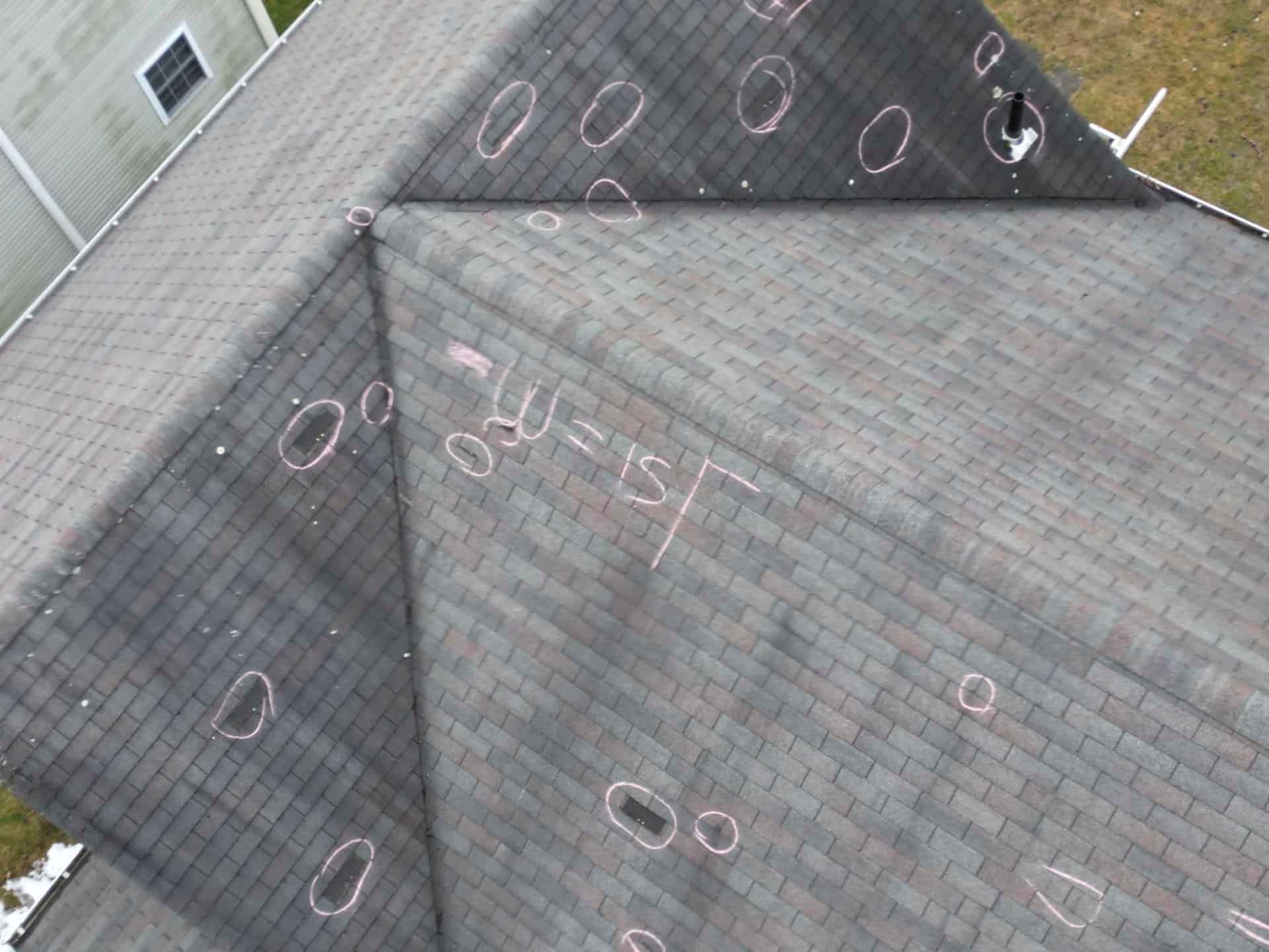 Aerial view of a gray shingled roof with chalk markings and several circular roof vents.