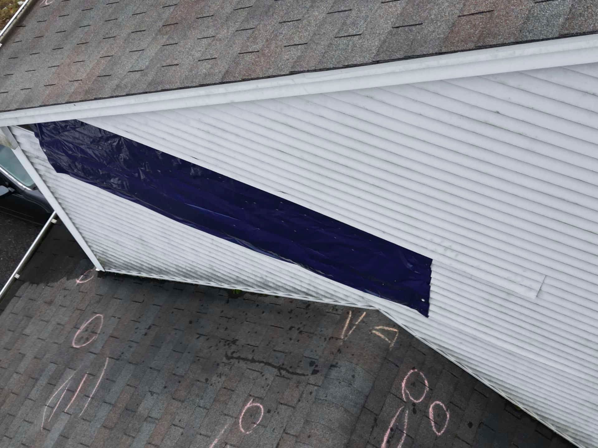 White house siding with a large dark blue diagonal panel and chalk markings on the pavement below.