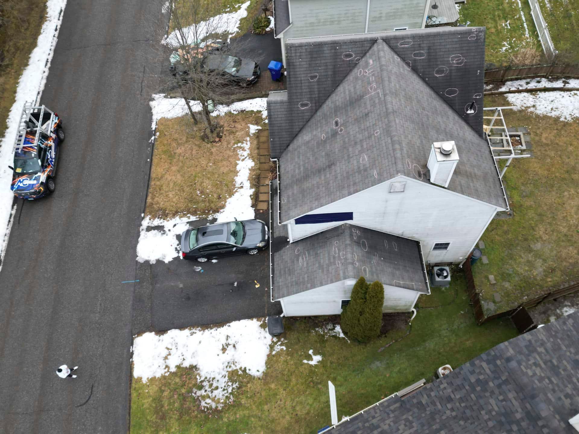 Aerial view of a house and driveway beside a road, with patches of snow and a parked car.