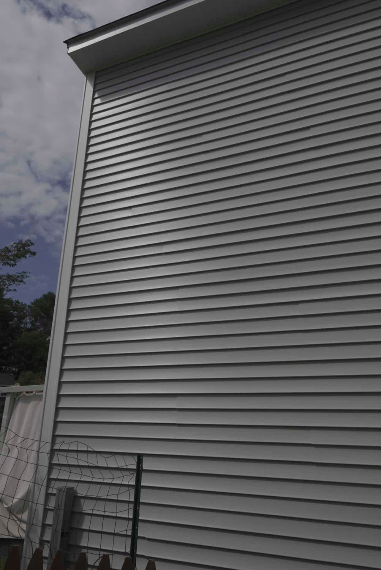 Gray vinyl-sided house exterior with a steep roofline and cloudy sky overhead