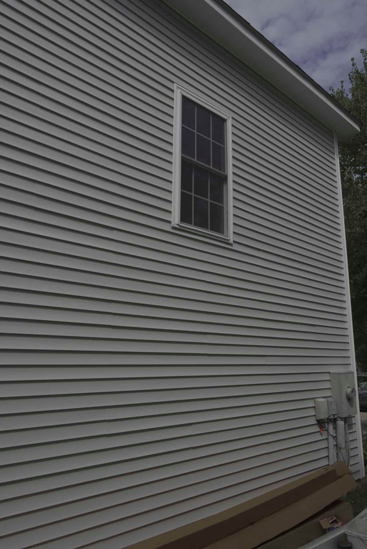 White house exterior with light gray vinyl siding and a single window.