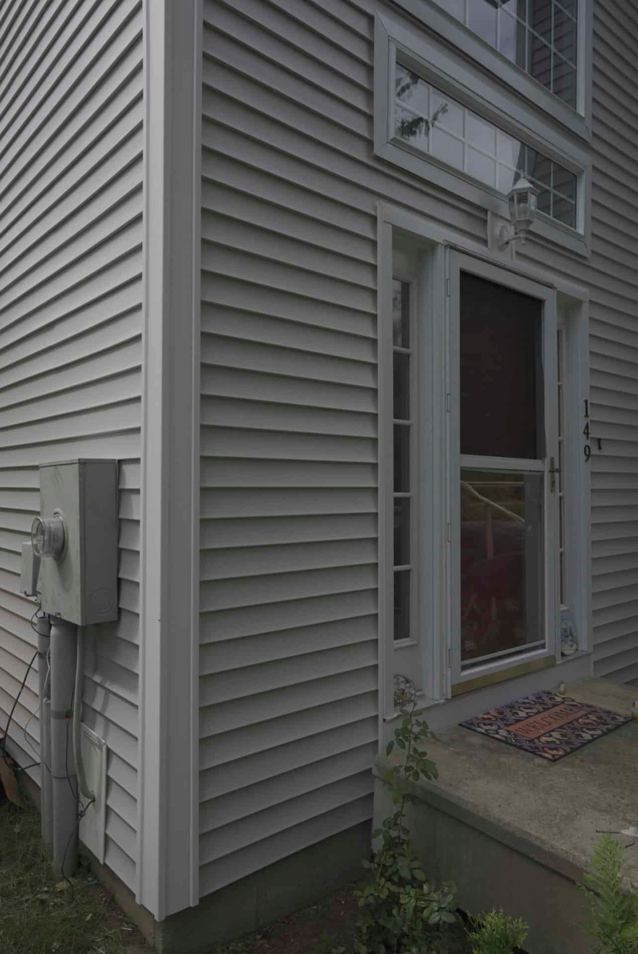 Side view of a gray house exterior with vinyl siding, a door, and a small concrete stoop.