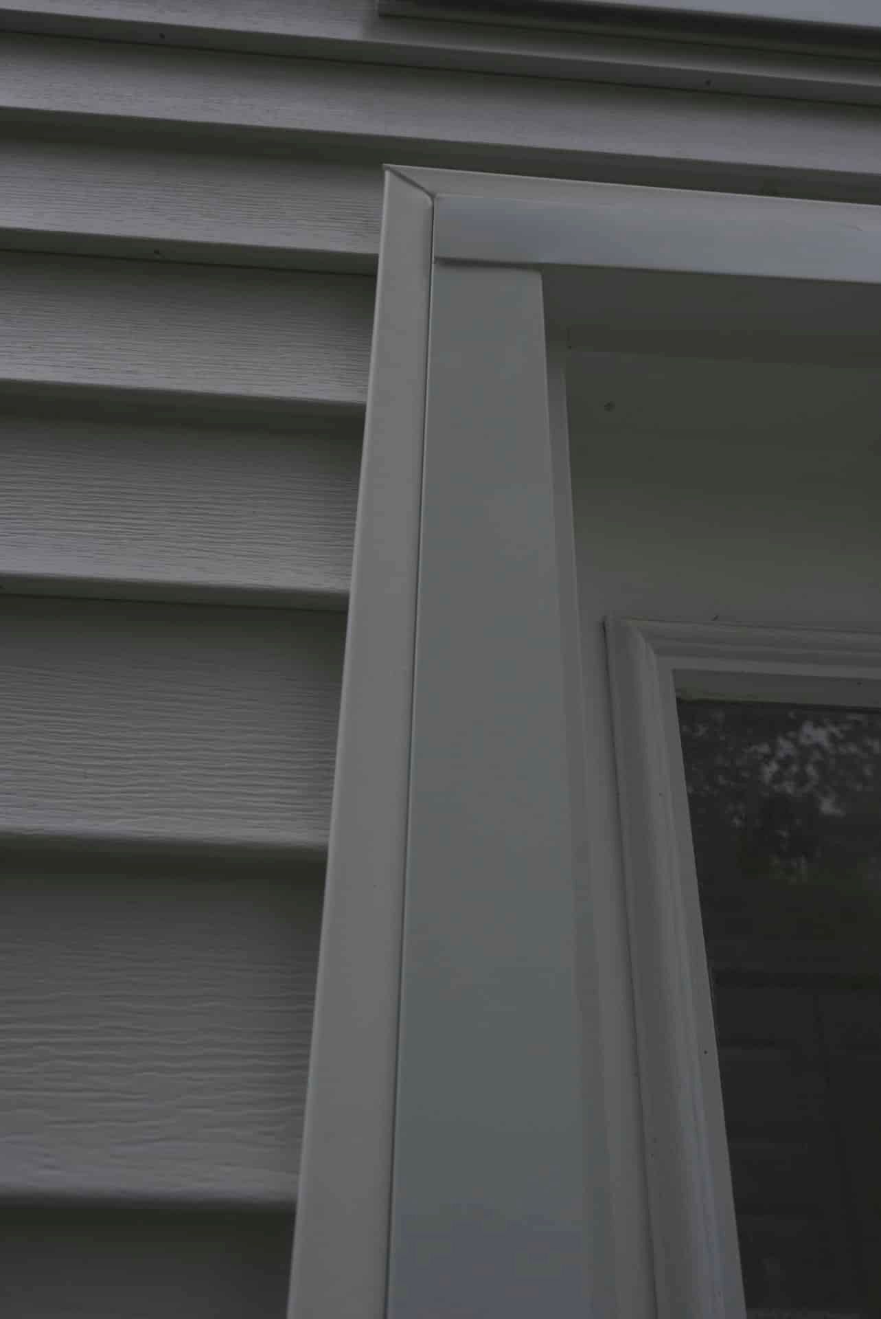 Close-up of white house siding and window trim beside a dark window.
