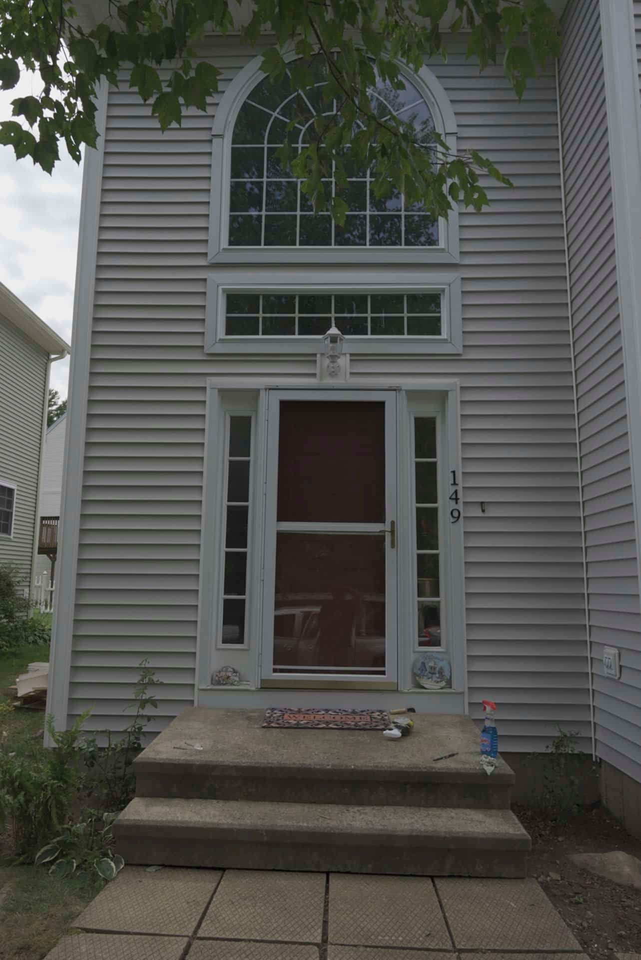 Narrow gray house facade with front steps, white-trim windows, and a small front porch after rain