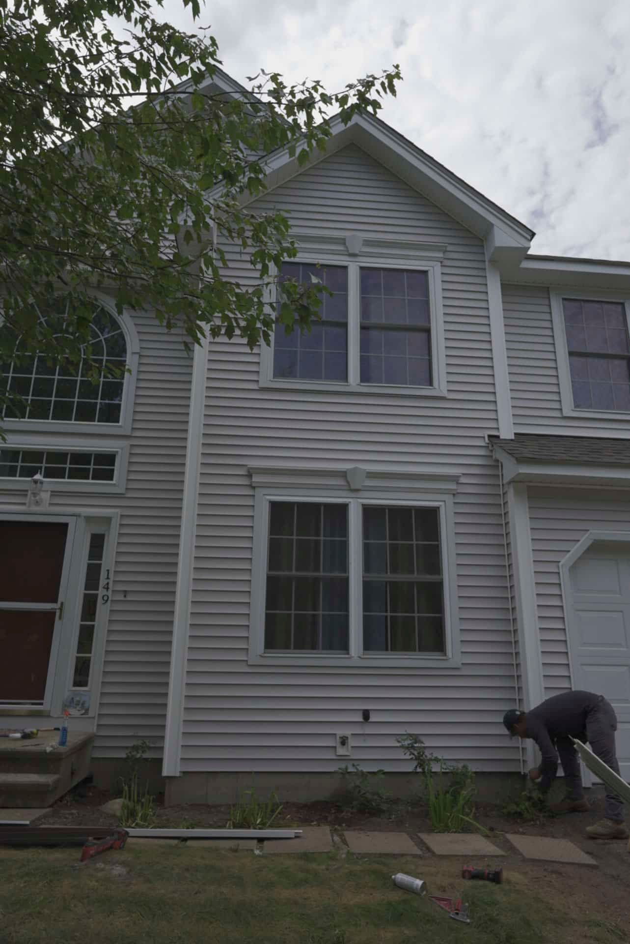 Side of a gray house with white trim, and a person bending over near the garden bed.