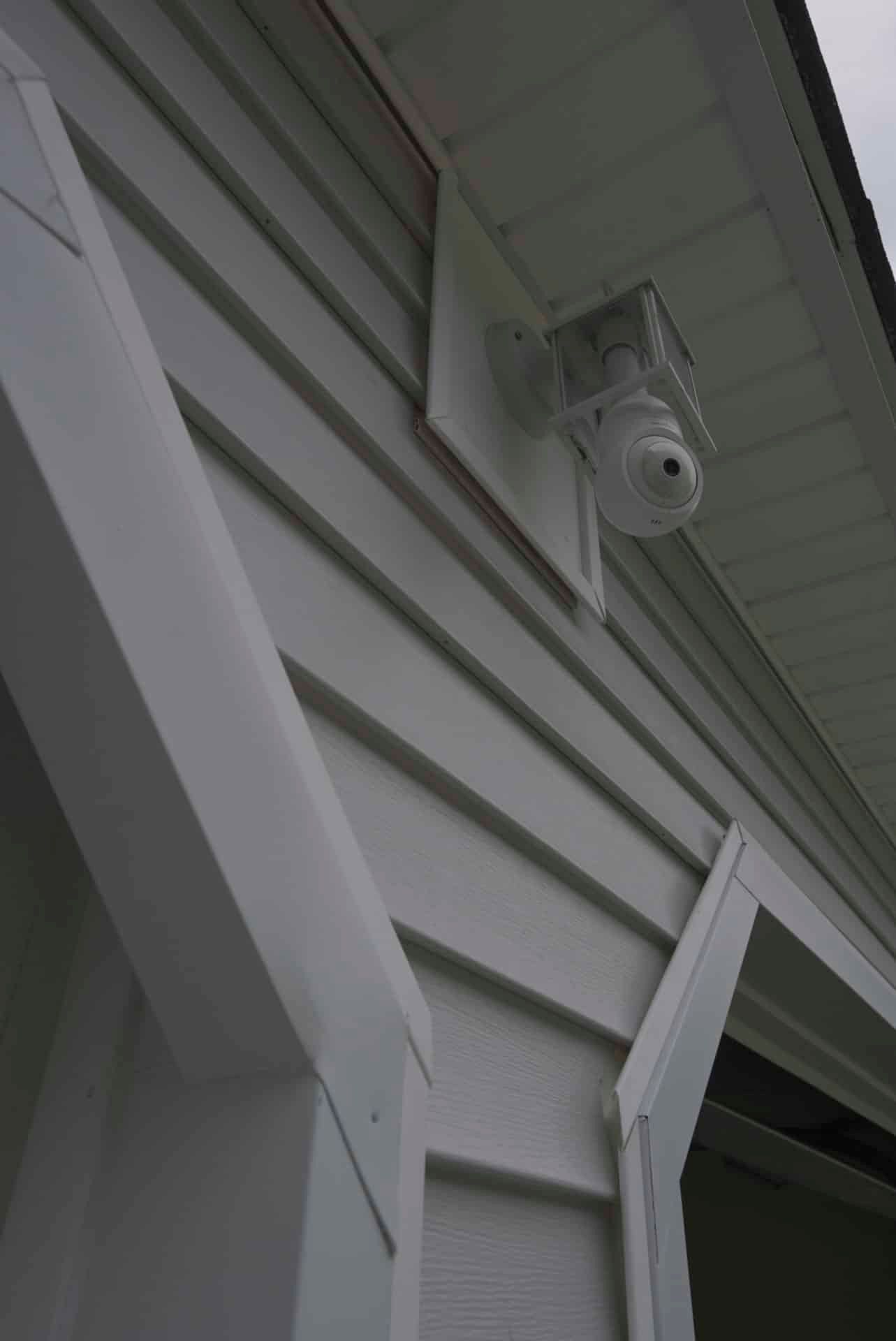 White house siding with a mounted security camera under the eaves above an open doorway
