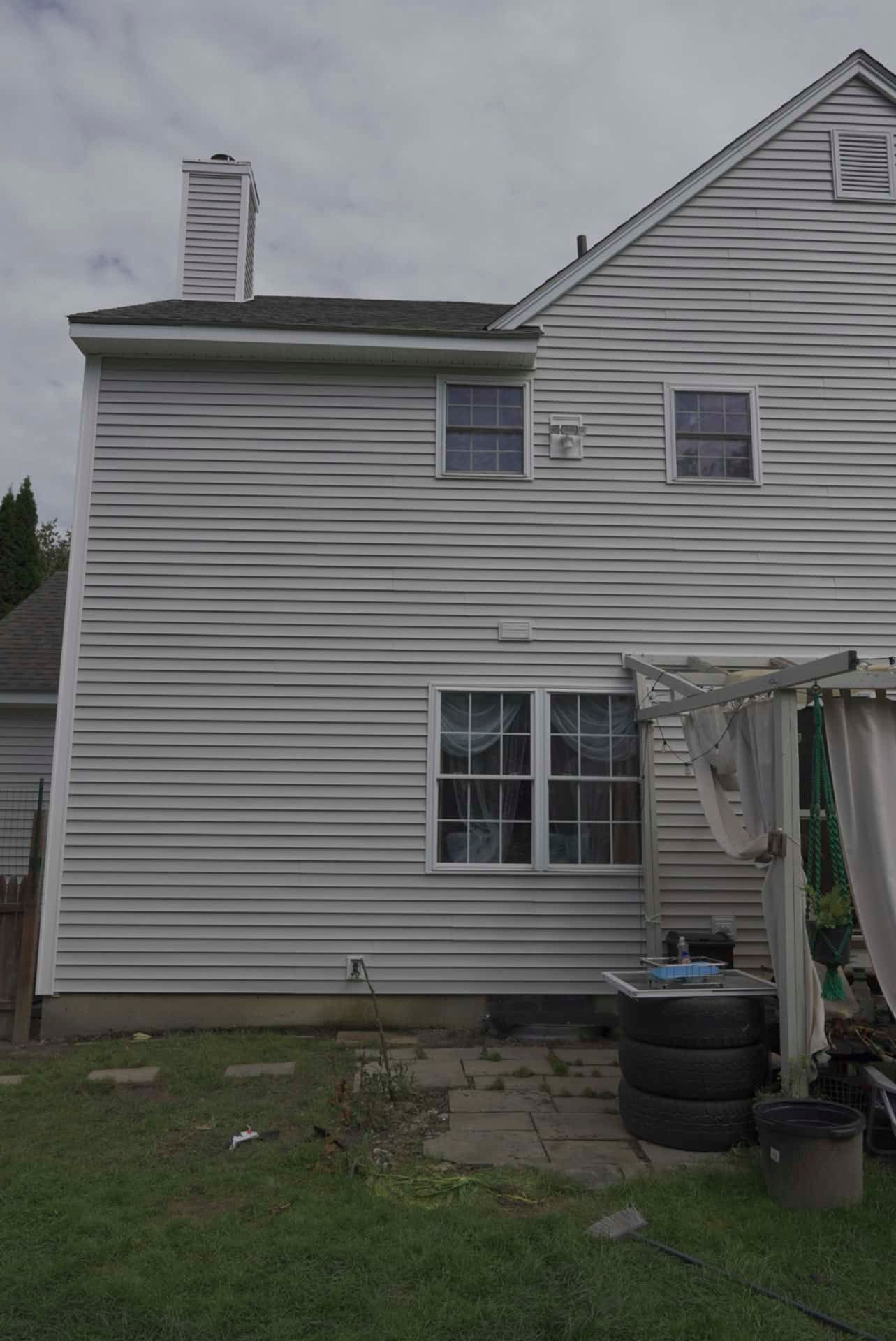 Back of a white house with a small patio, grass yard, and stacked tires near the door