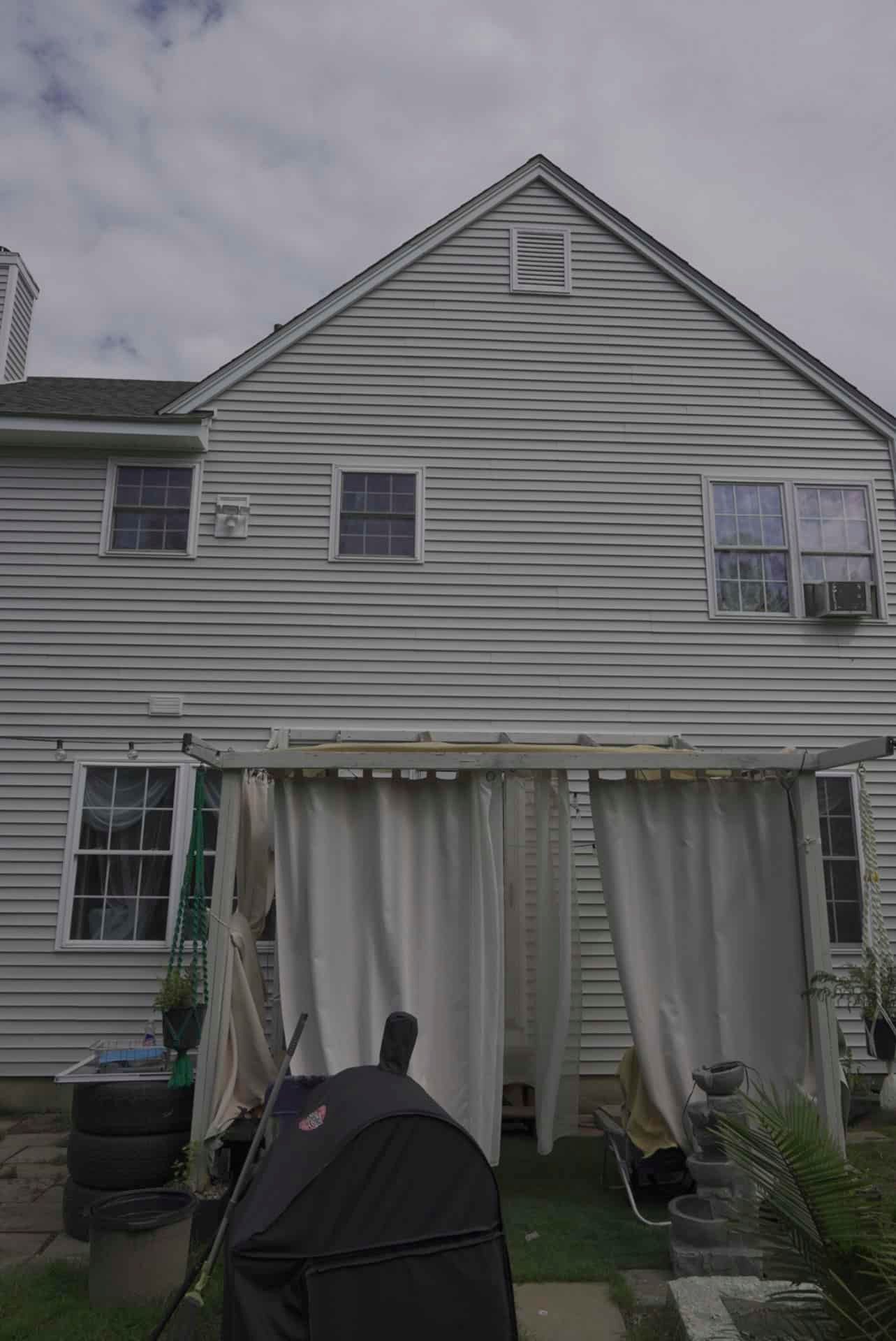 Gray two-story house with striped siding and a covered patio, viewed from the backyard.
