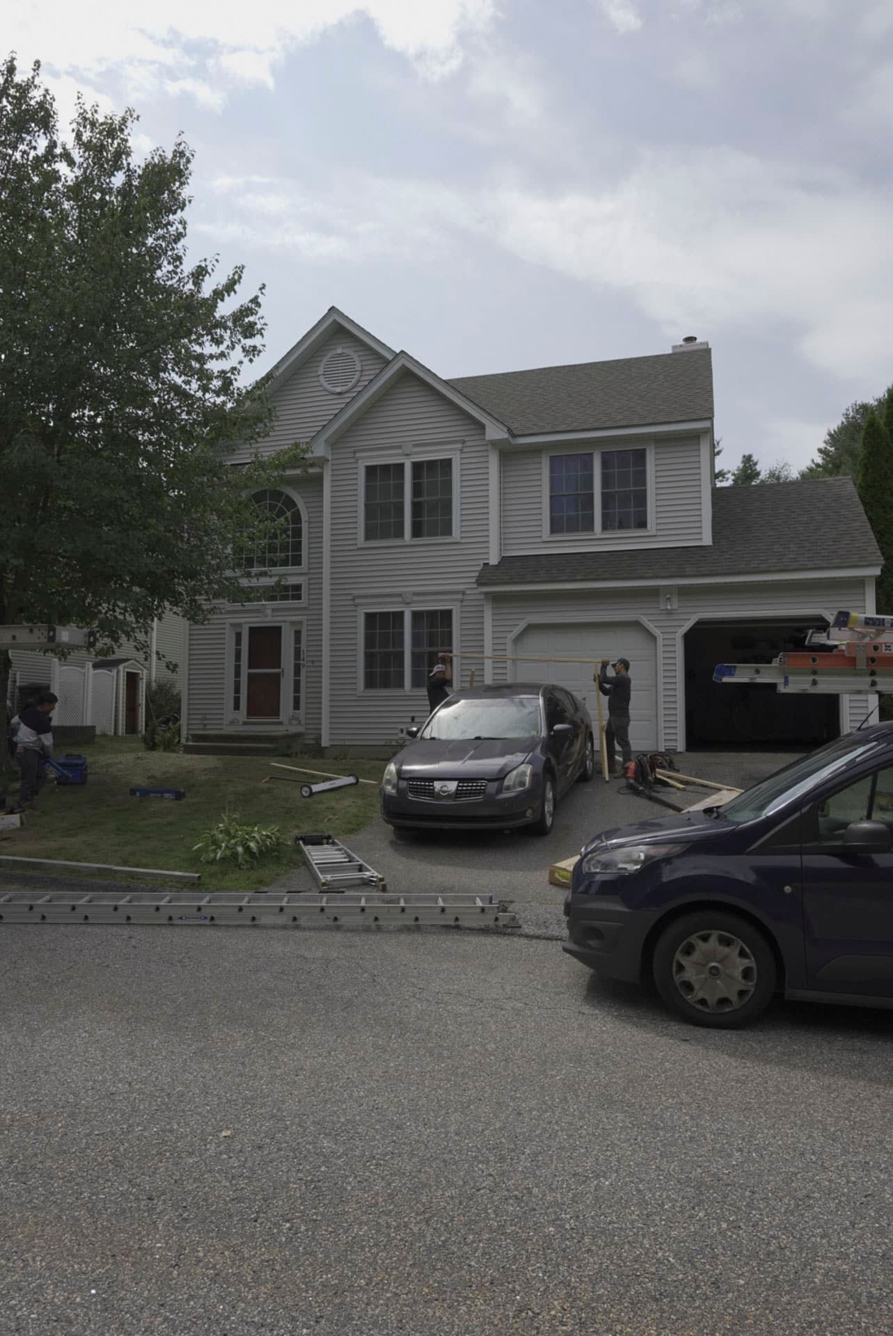 Suburban two-story house with two parked cars and a garage, viewed from the street.