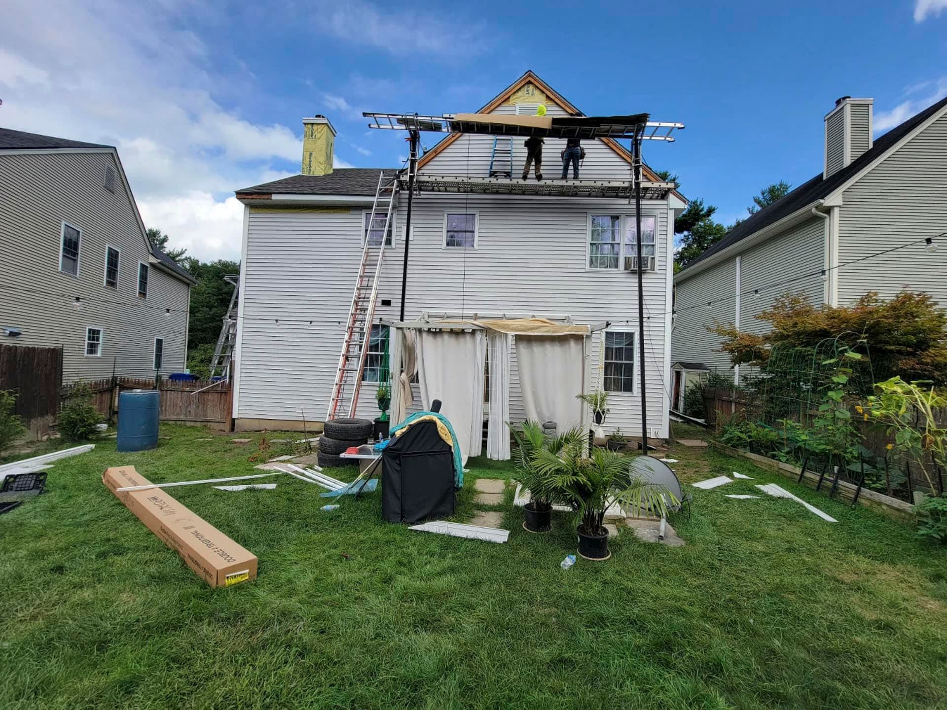 House exterior with scaffold and ladder during roof repair in a grassy backyard