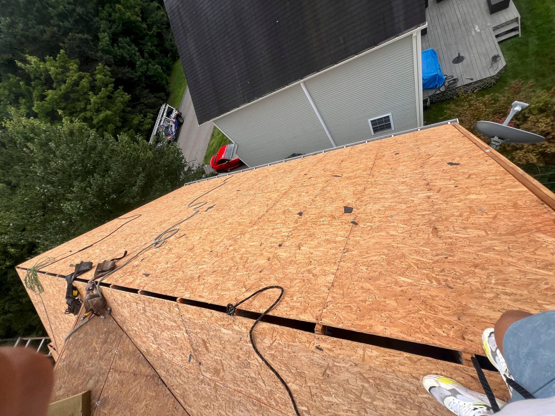 Roofing plywood on a house roof with a safety rope and nearby tools.