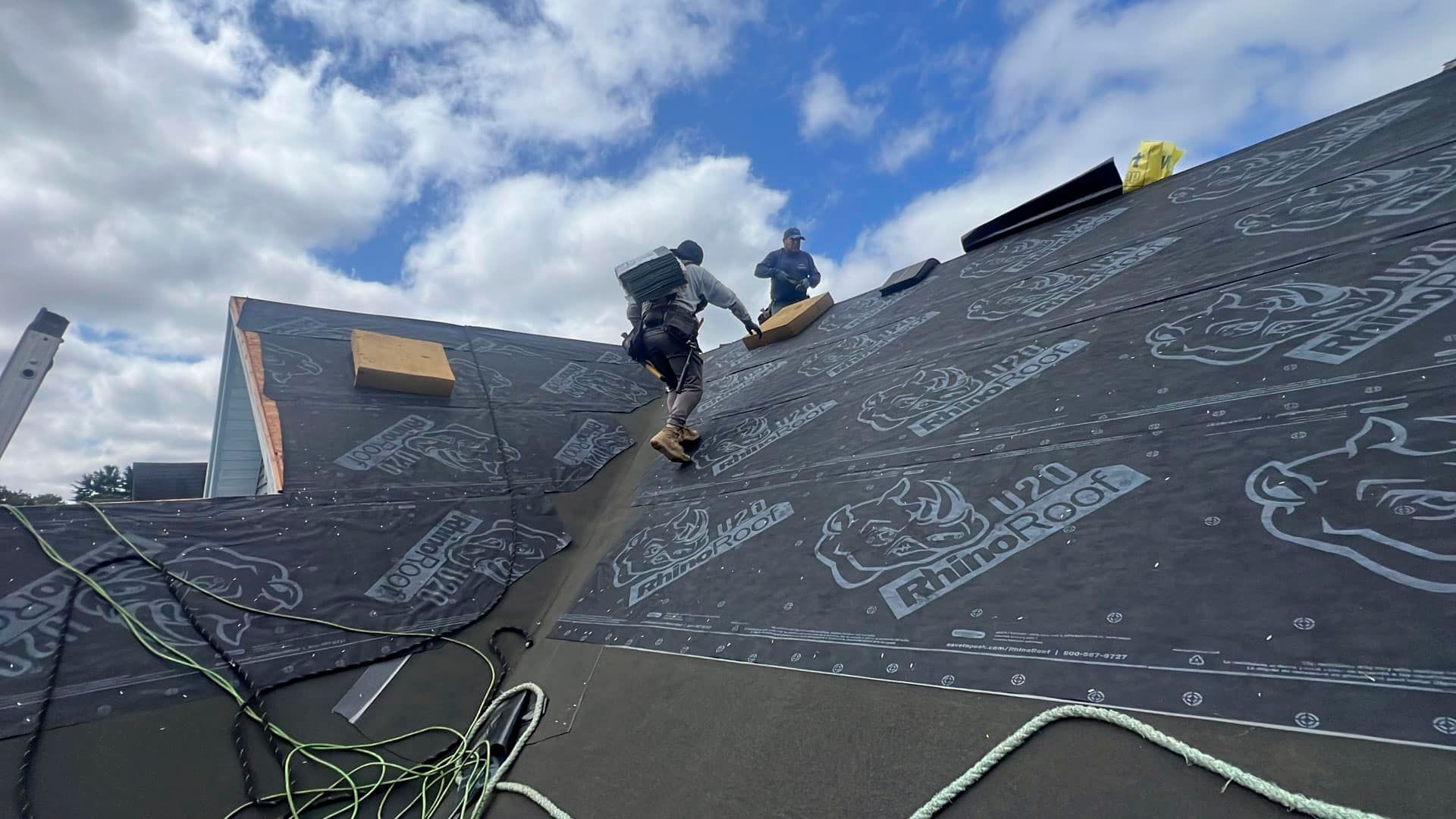Workers on a steep roof under construction, covering it with black underlayment and chalk markings.