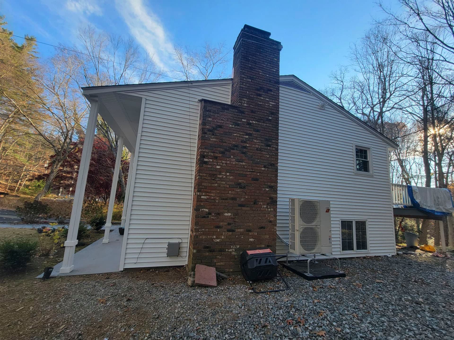 Back view of a white house with brick chimney, gravel yard, and HVAC units under a blue sky