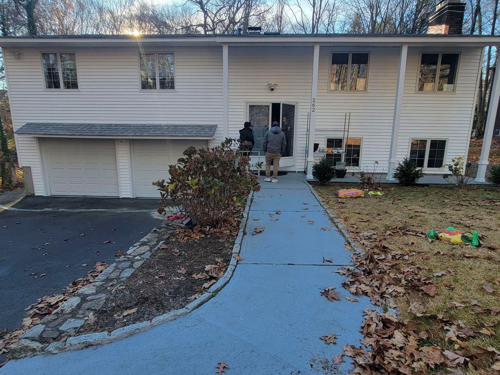 Two-story suburban house with a driveway, walkway, and autumn leaves on the lawn.