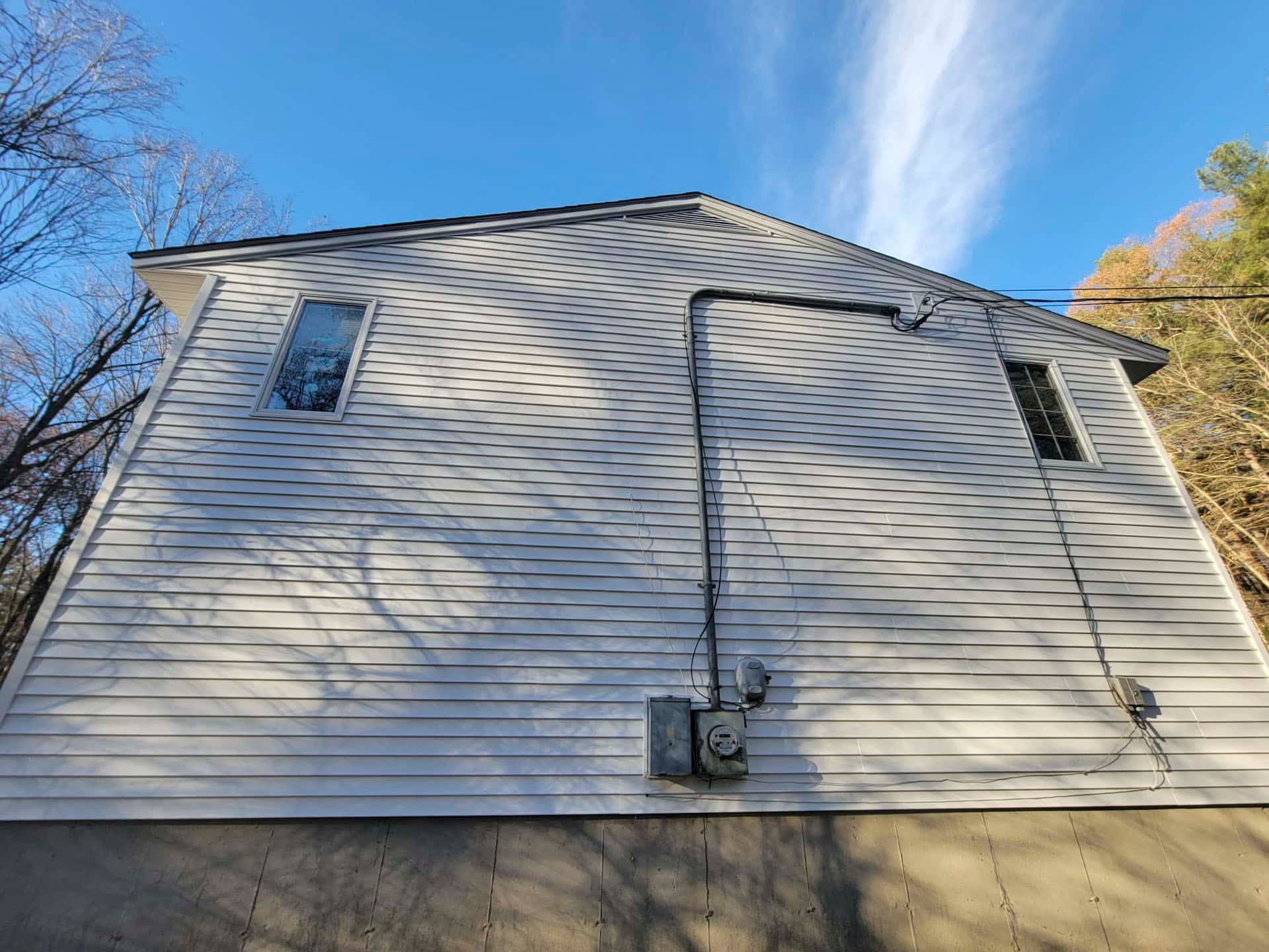 Side of a beige vinyl house with two small windows and a utility meter under a blue sky