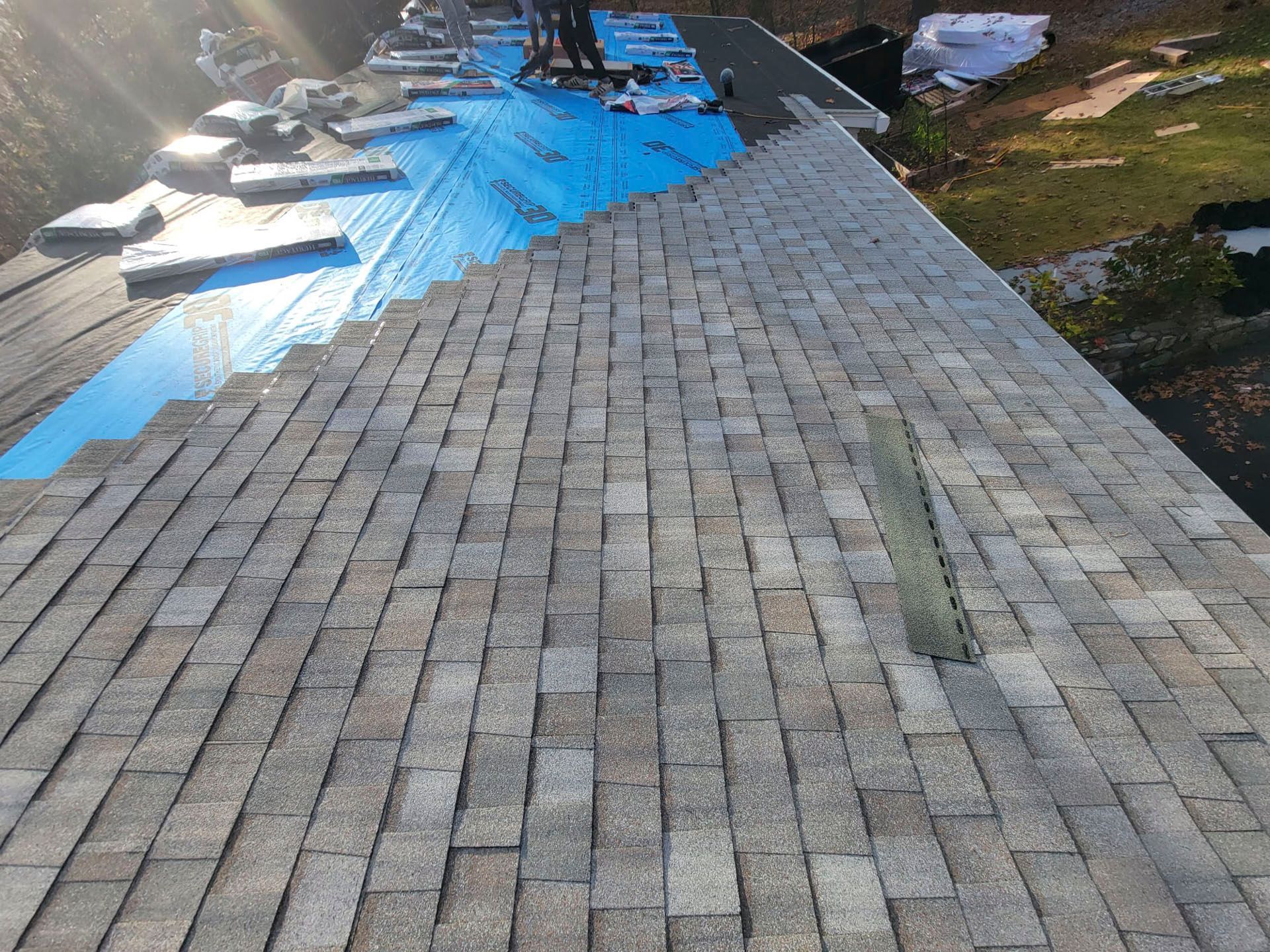 Rooftop covered with gray shingles and blue tarp, viewed from above after storm damage