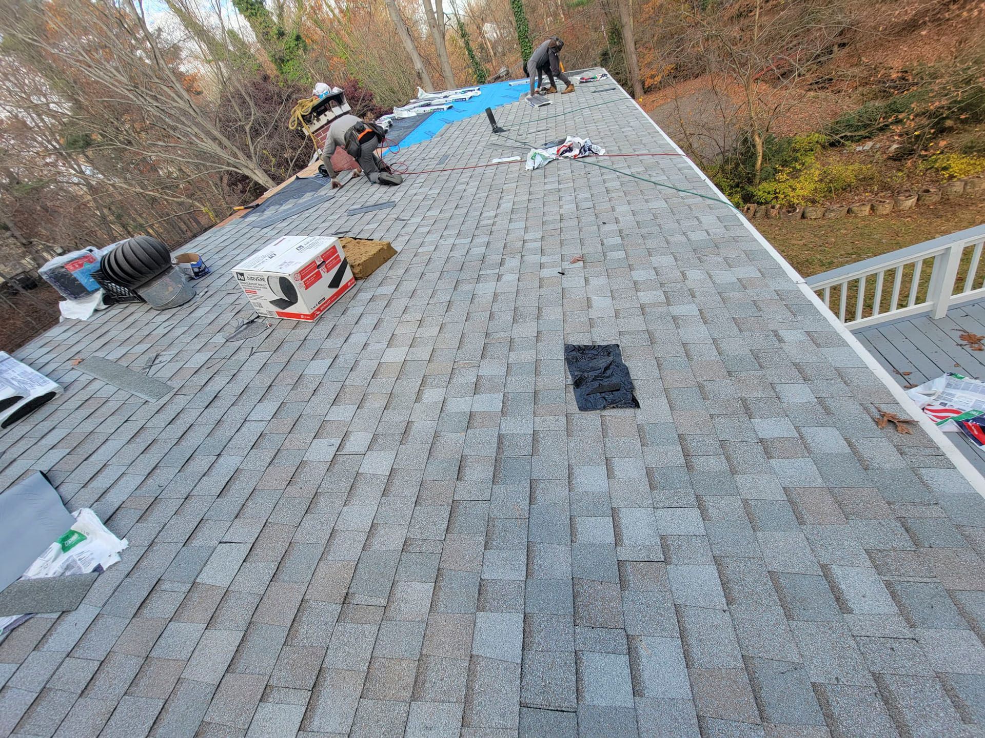 Workers installing gray shingles on a sloped roof with tools and materials scattered around.