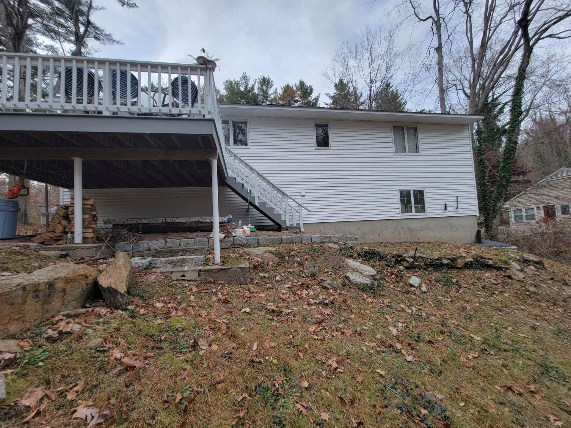 White house side wall badly bowed and damaged beside a raised deck in a leaf-covered yard