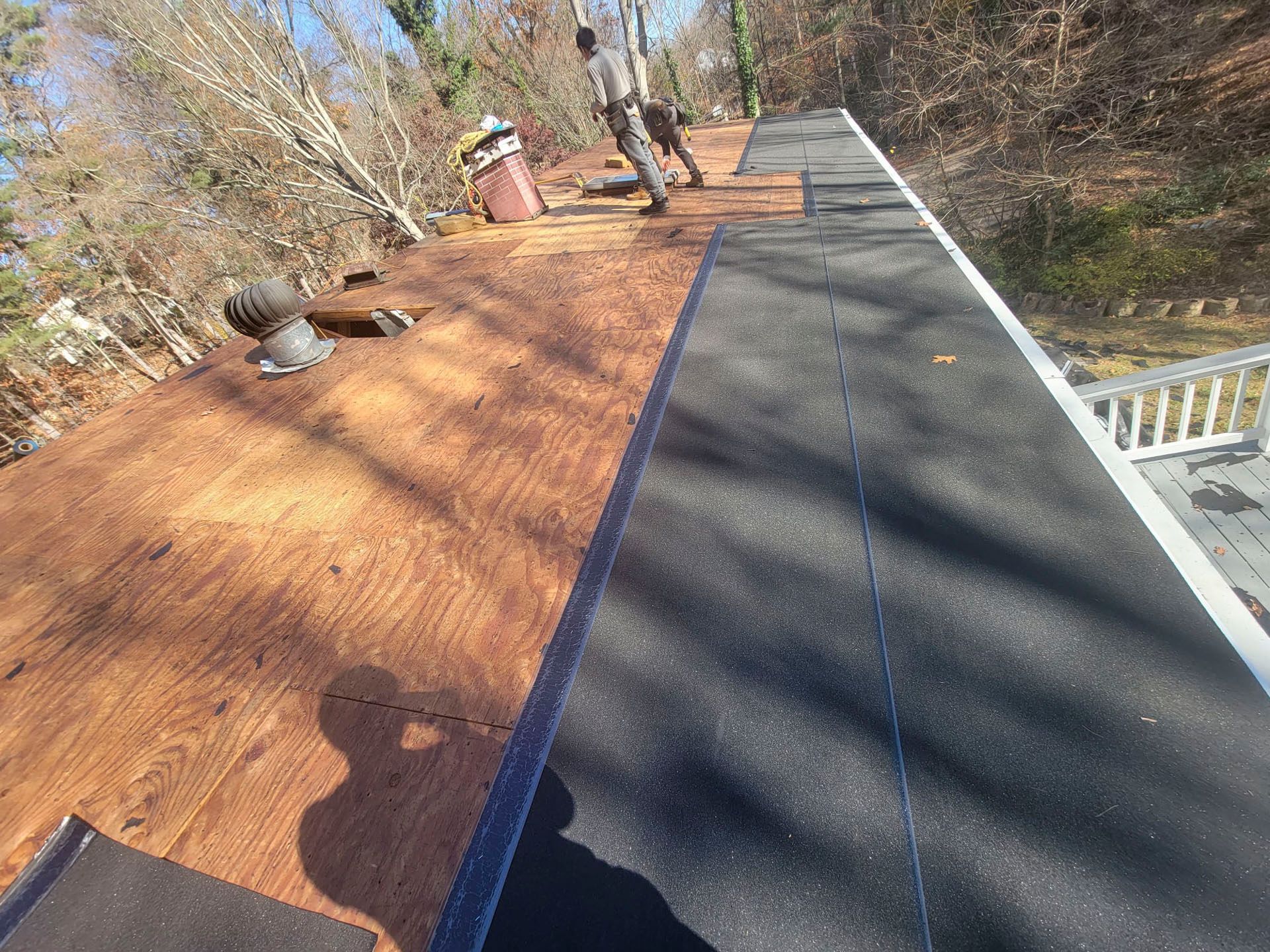 Roof under construction with red underlayment on one side and black shingles on the other, workers in the distance