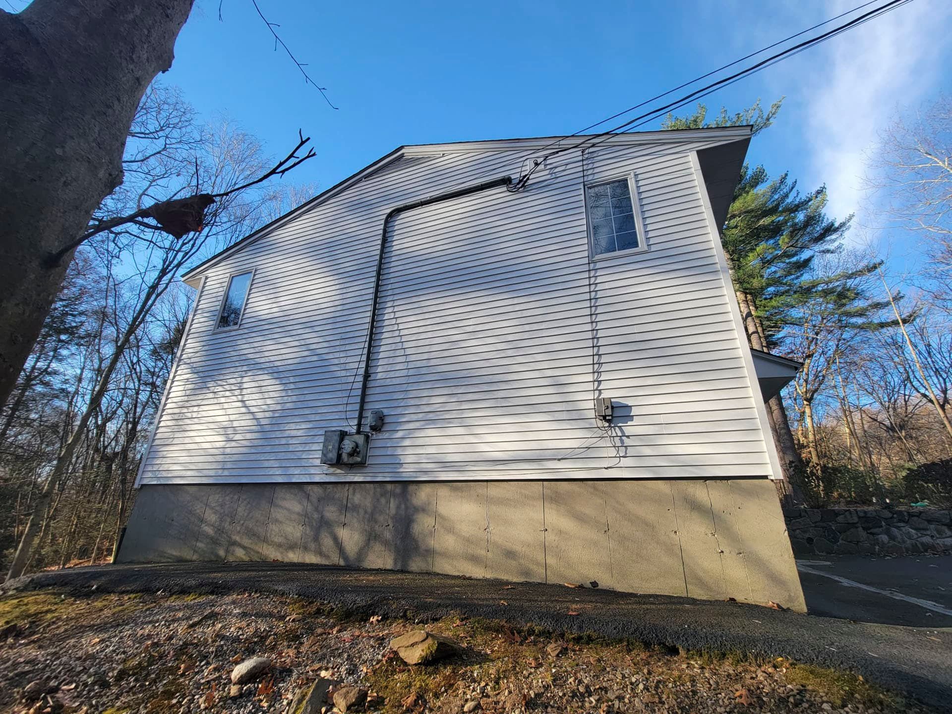White house exterior with beige foundation, blue sky, bare trees, and an overhead power line